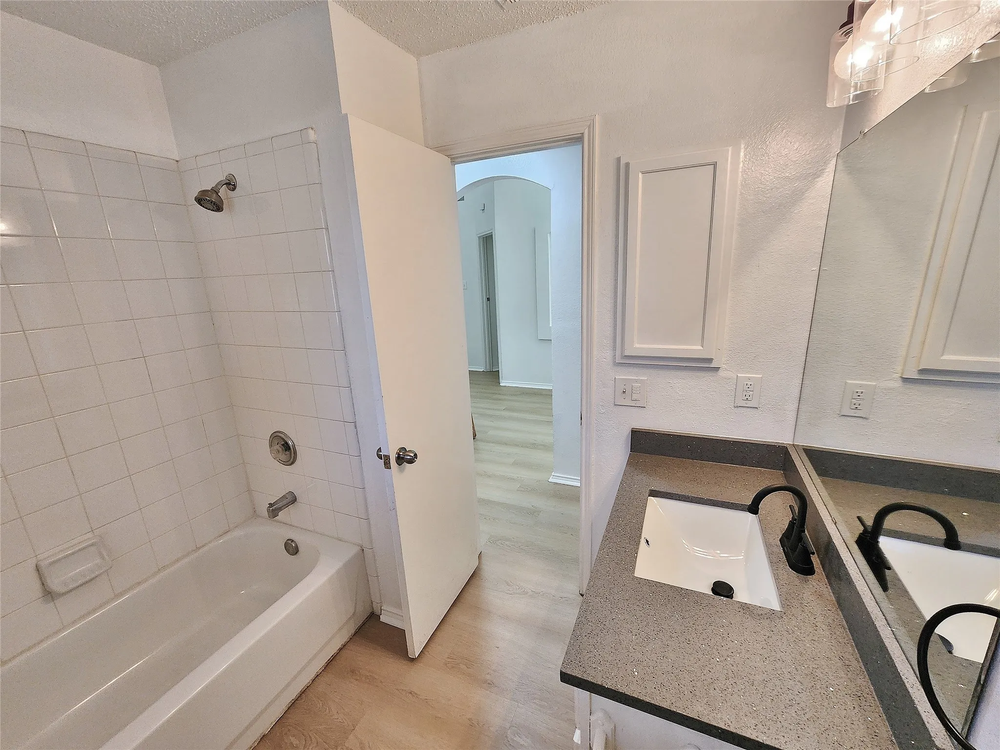 Full bathroom featuring a tub/shower combination with white tile surround, a single vanity with a dark countertop, and wood-finish flooring