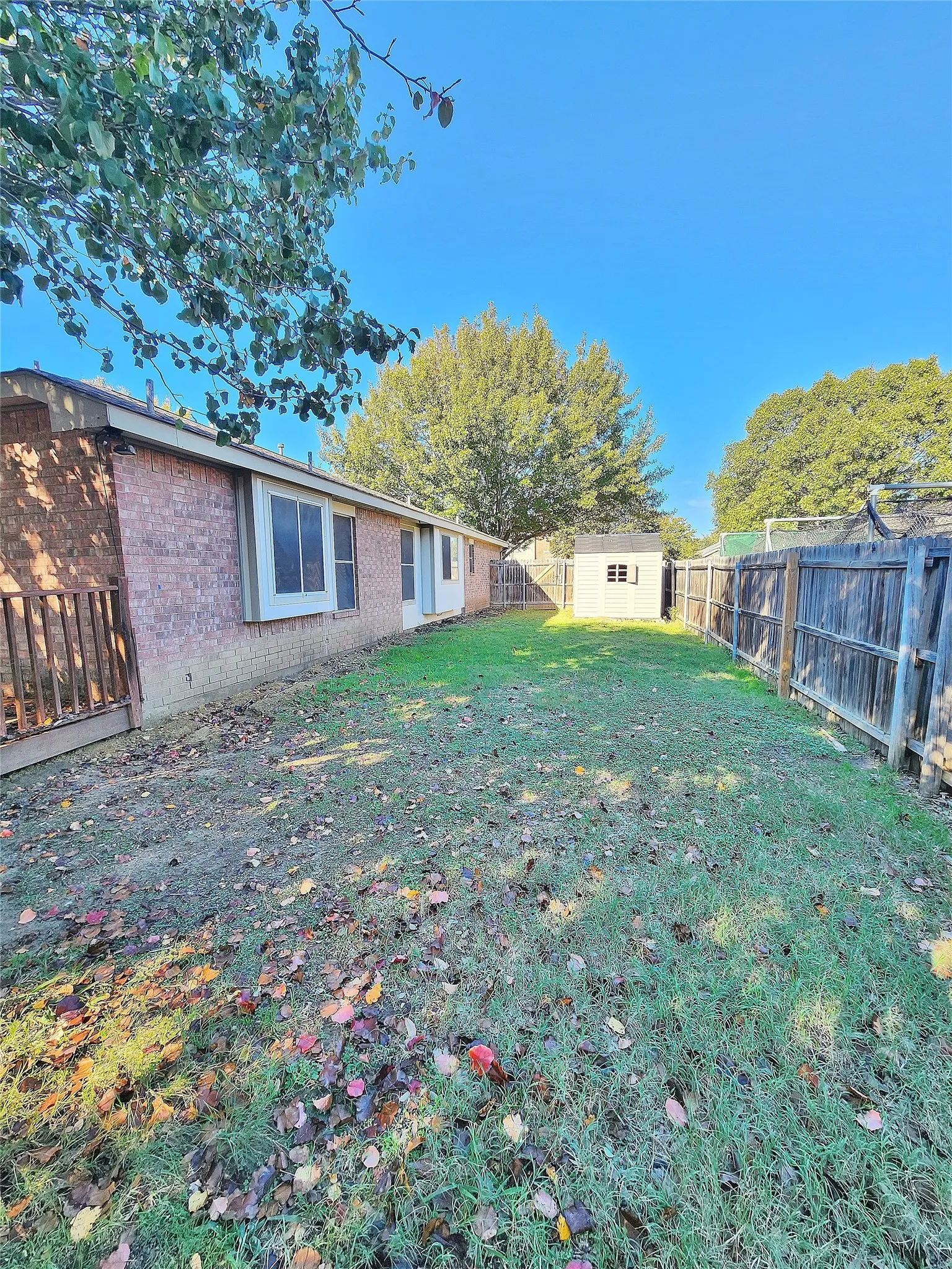 Expansive grassy area featuring a wood fence, storage shed, and mature trees