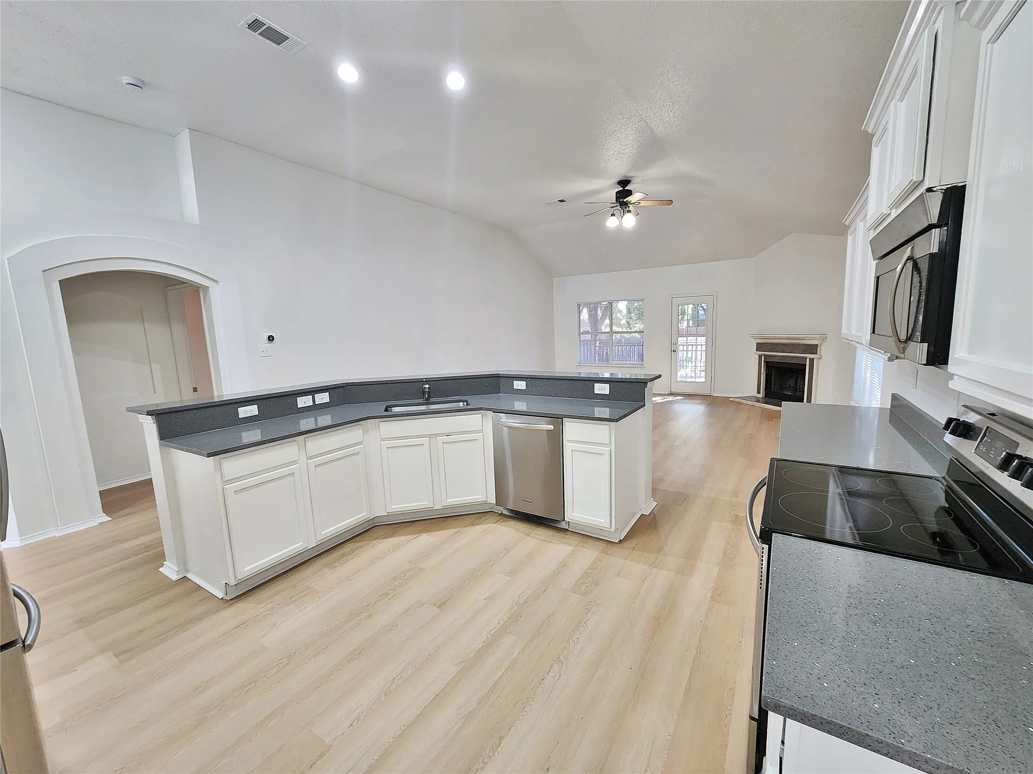 Open-concept kitchen featuring white cabinetry, gray countertops, stainless steel appliances, and wood-finish flooring