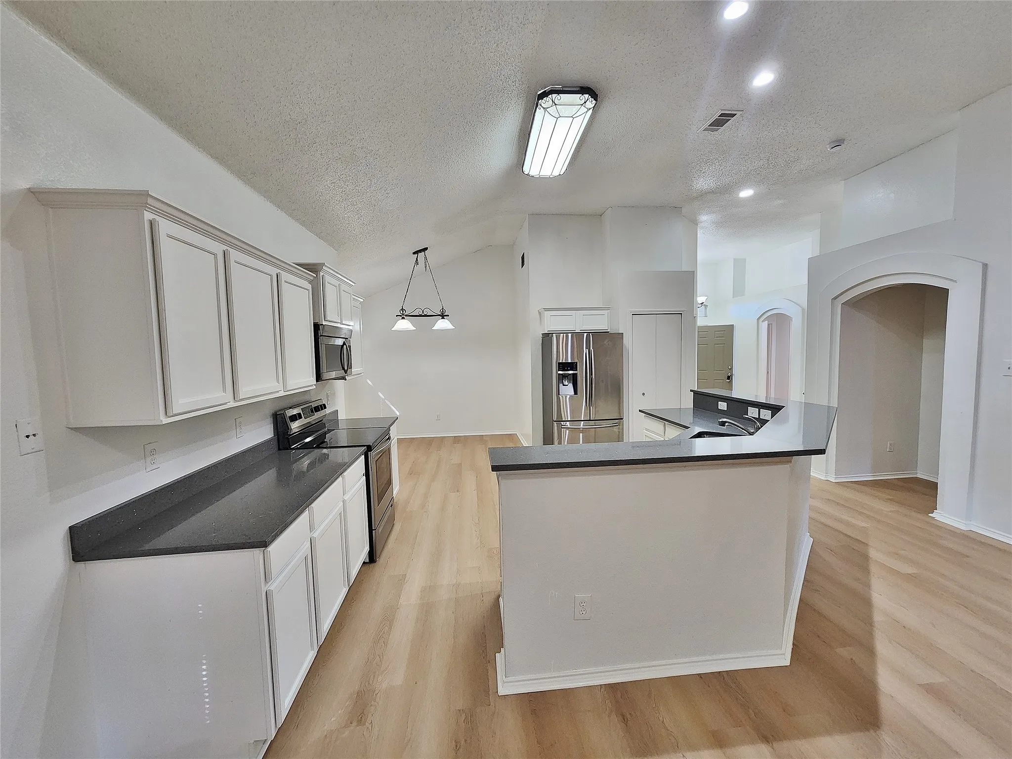 Kitchen featuring white shaker-style cabinetry, dark countertops, stainless steel appliances, and wood-finish flooring