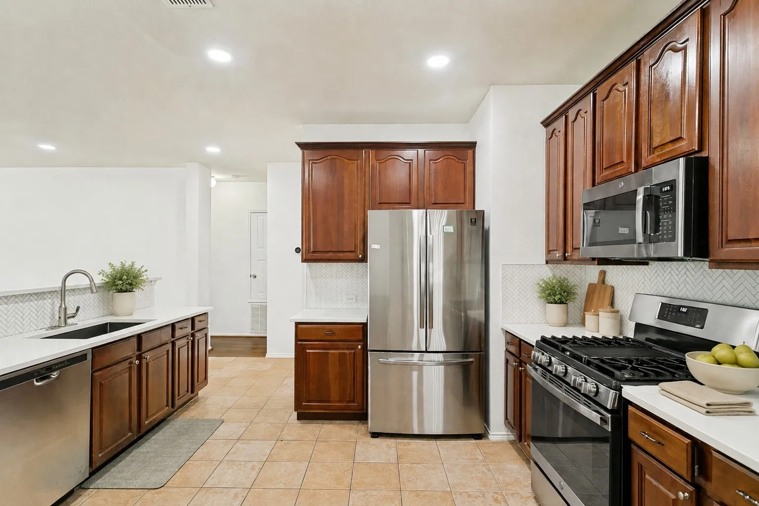 Kitchen featuring stainless steel appliances, wood cabinetry, light countertops, and a herringbone tile backsplash
