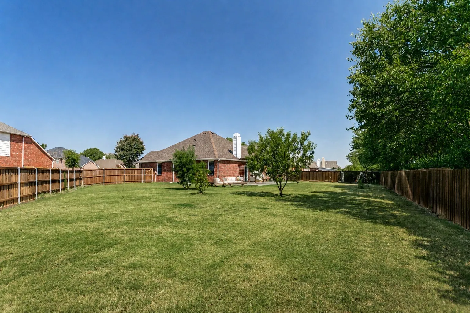 Expansive backyard with a manicured lawn, full wood fencing, and mature trees