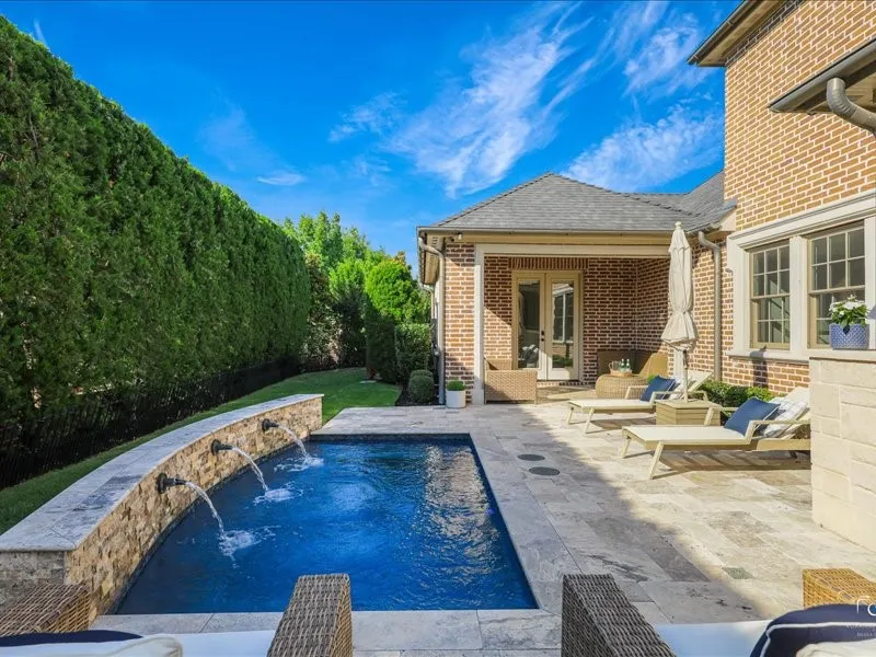 Outdoor living area featuring a rectangular plunge pool with an integrated stone water feature, a stone tile patio, and a covered porch