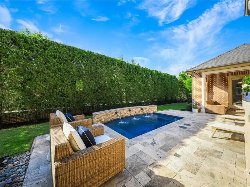 Backyard oasis featuring a rectangular swimming pool with three water spouts and a stone-tiled patio