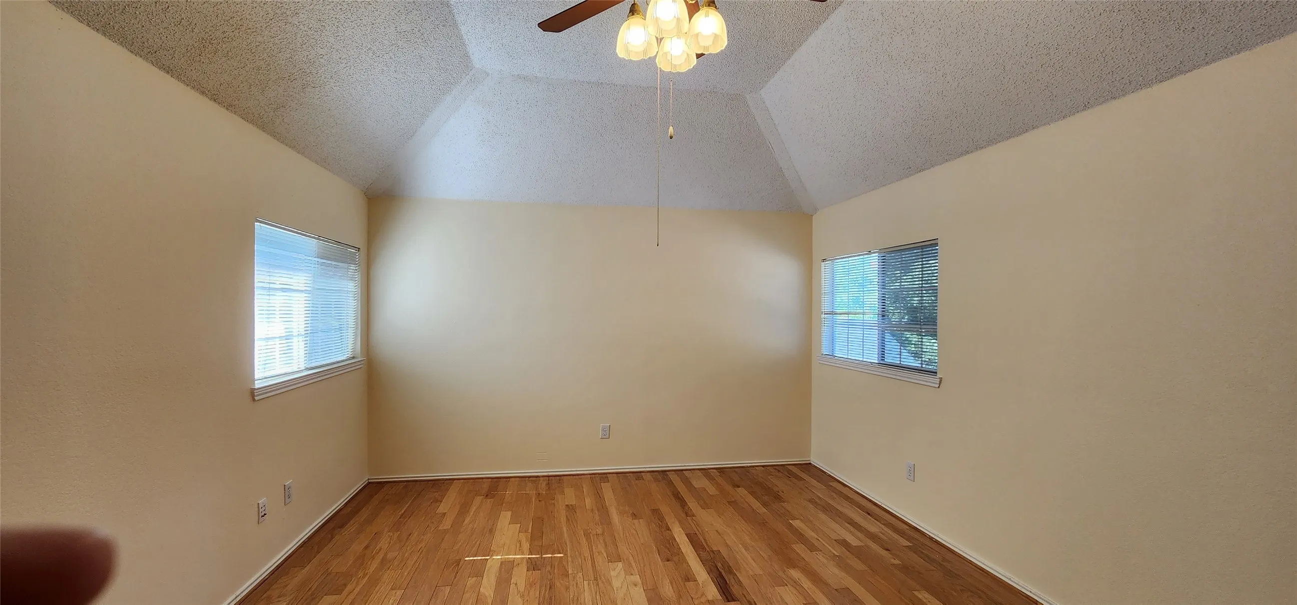 Vaulted ceiling with a ceiling fan light fixture, light wood-finish flooring, and two windows