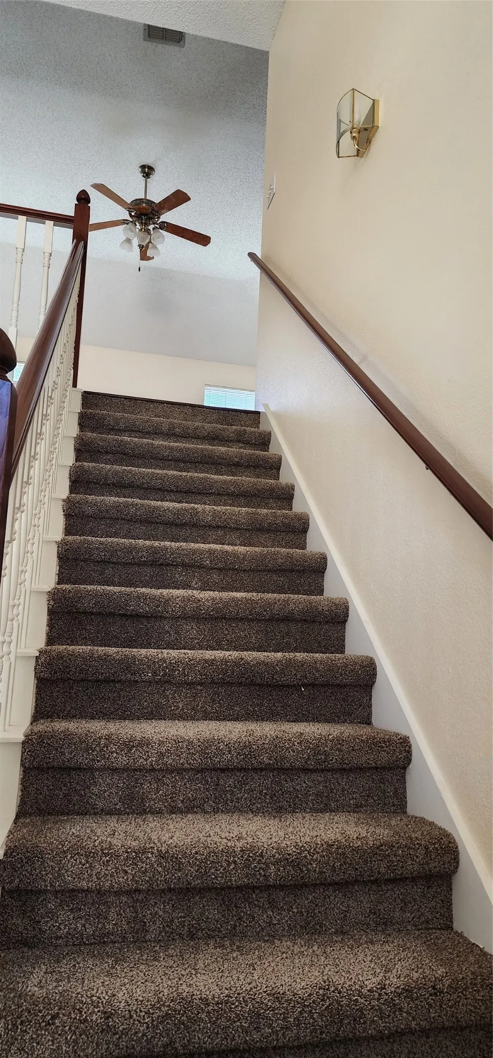 Carpeted staircase with a wood-finish handrail and integrated ceiling fan