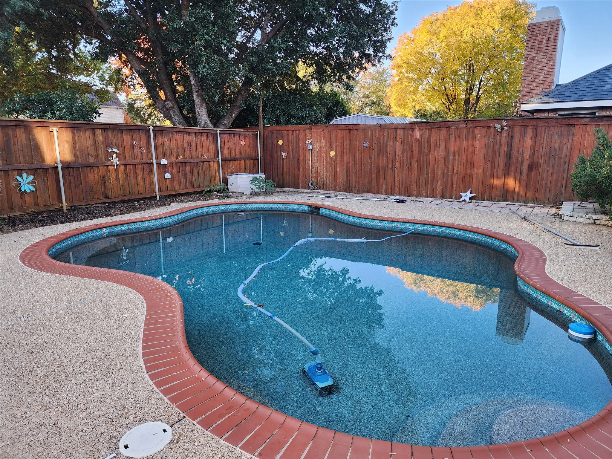 Freeform swimming pool with a brick coping, textured deck surround, and a stained wood privacy fence