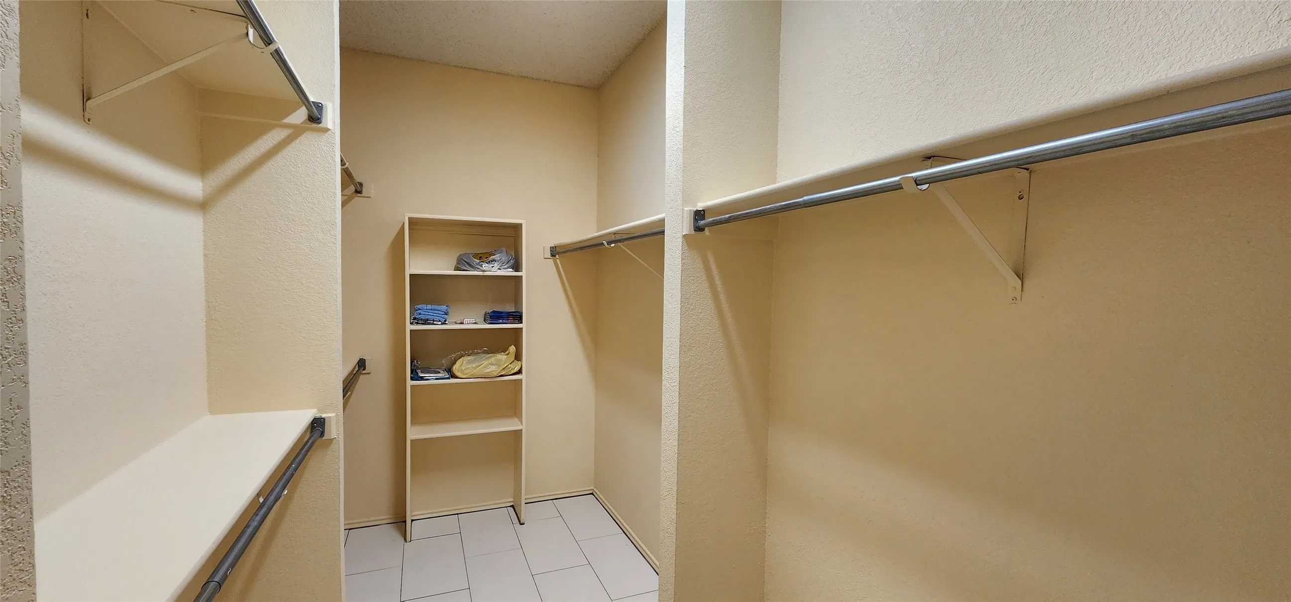 Walk-in closet with multiple hanging rods, integrated shelving unit, and light-toned tile flooring