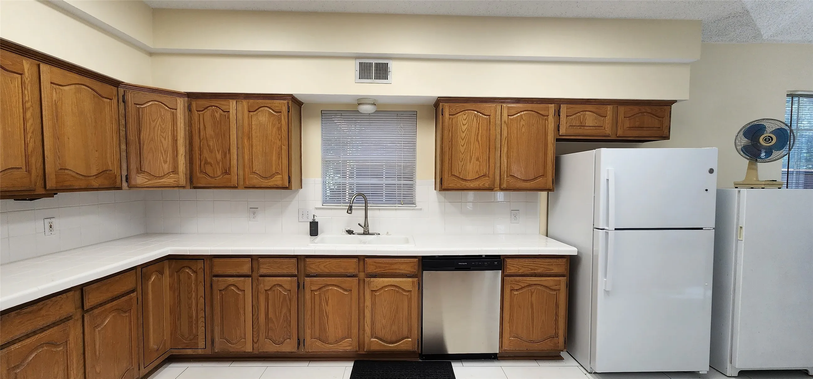 Kitchen featuring wood cabinetry, white countertops, white tile backsplash, and a stainless steel dishwasher