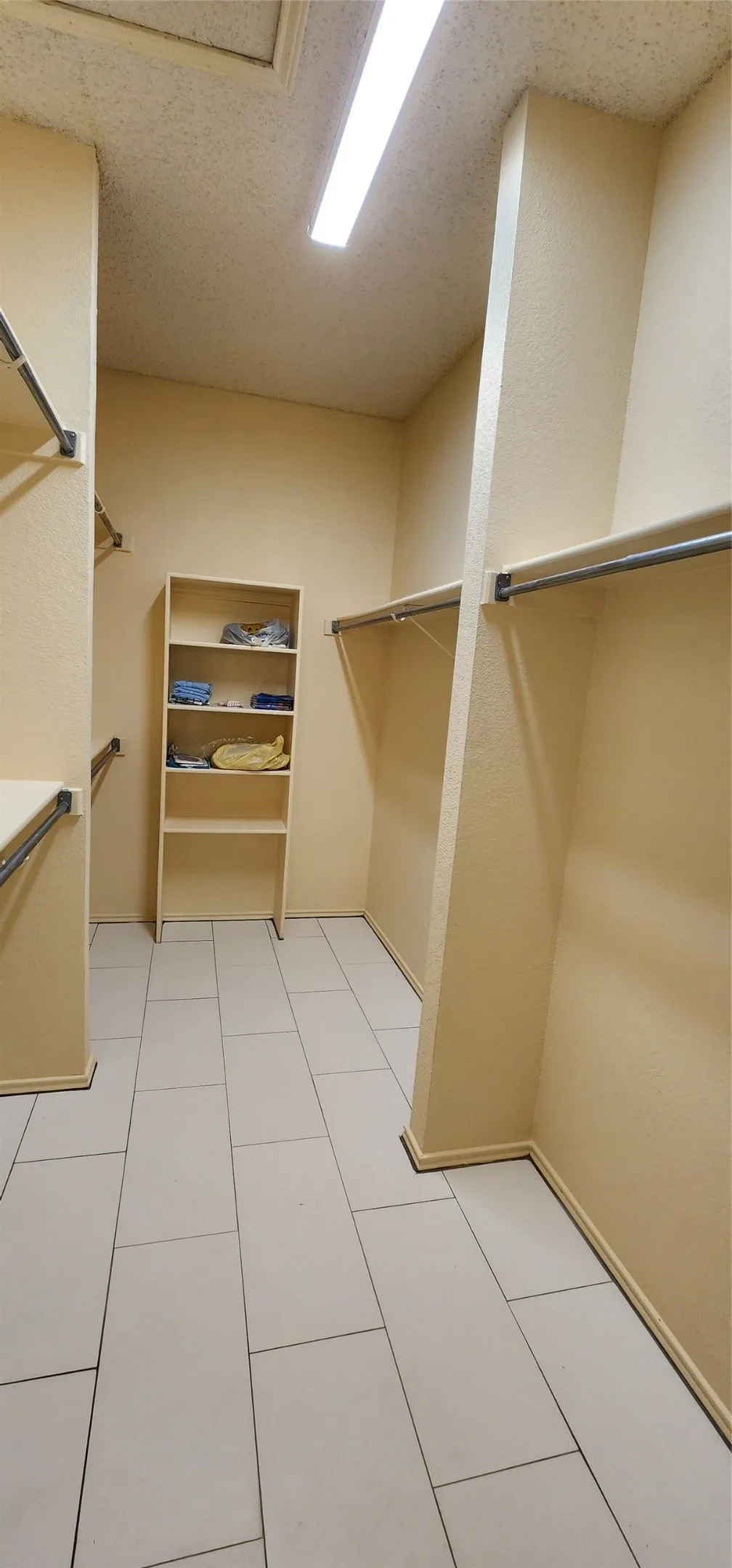 Walk-in closet featuring light-toned walls, tile flooring, built-in shelving, and metal hanging rods