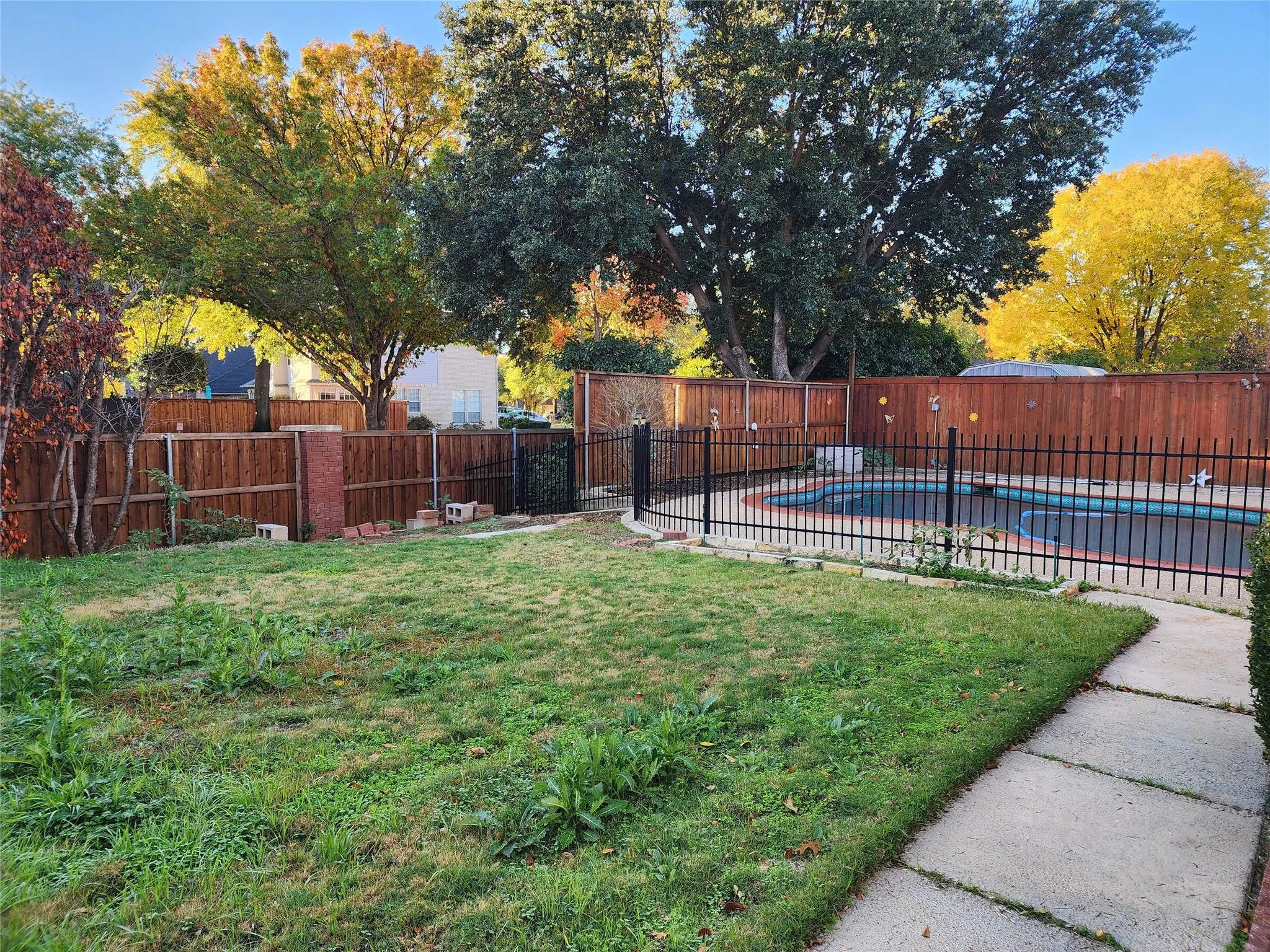 Expansive backyard with a concrete pathway, wood fence perimeter, and a fenced swimming pool