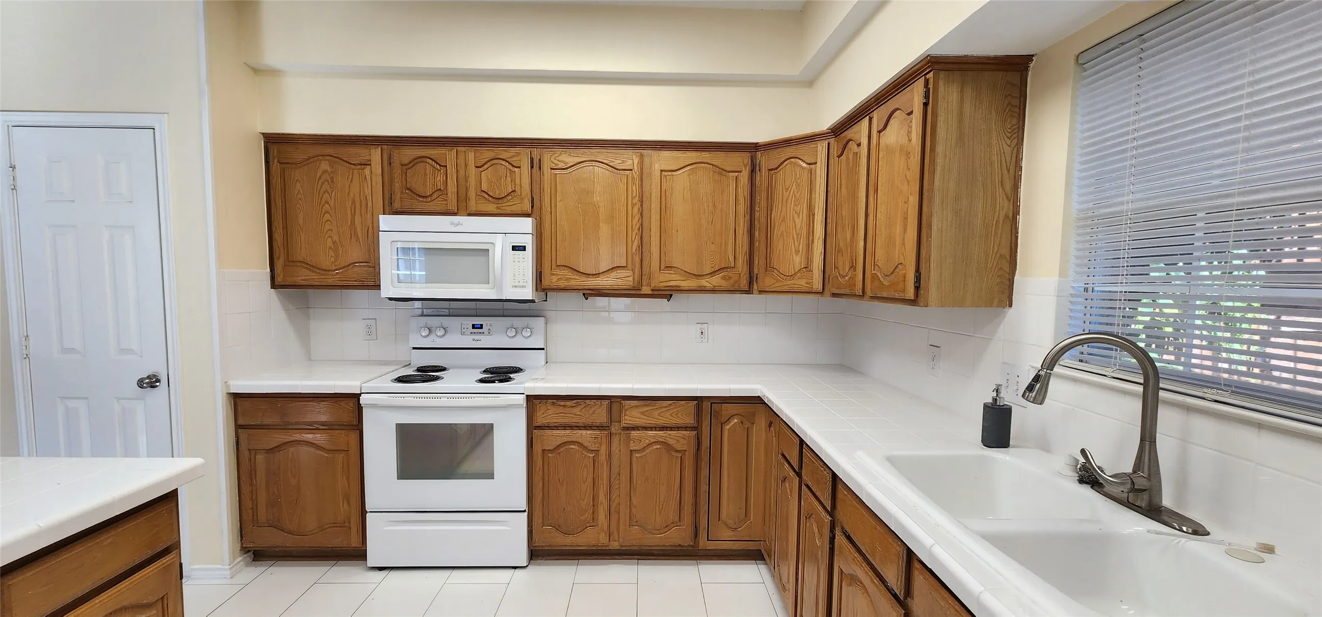 U-shaped kitchen featuring wood-finish cabinetry, white countertops, white tile backsplash, and an integrated white sink with a gooseneck faucet