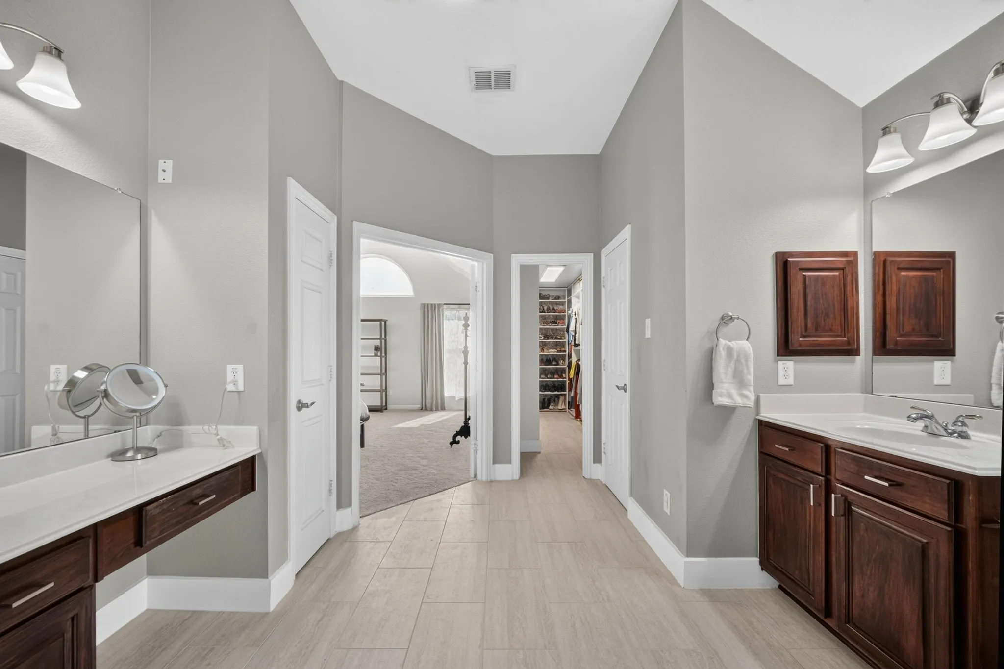 Vaulted ceiling bathroom with dual dark wood-finish vanities, light countertop, and tile flooring