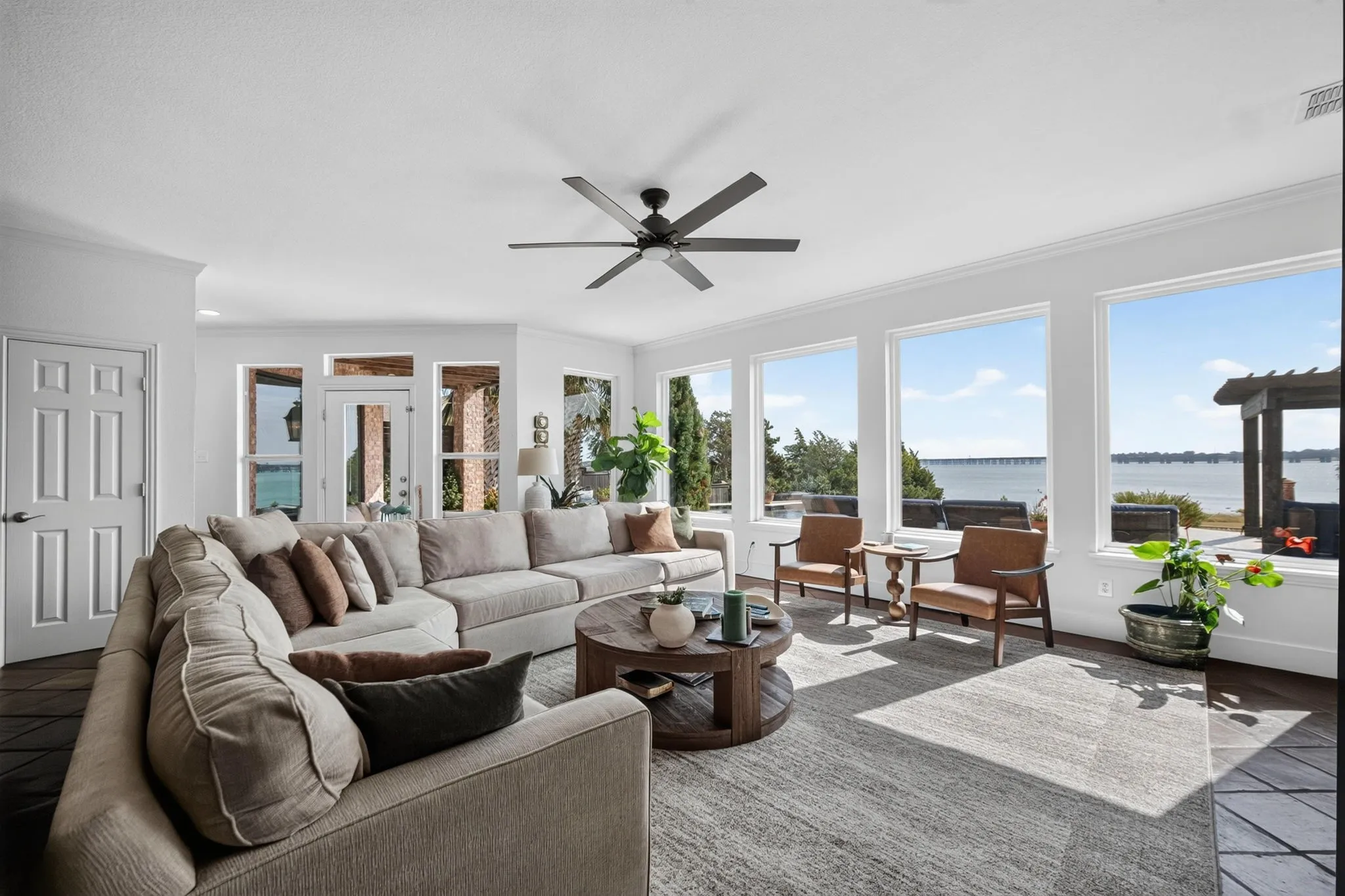 Spacious living area featuring expansive windows, beautiful flooring, and a ceiling fan