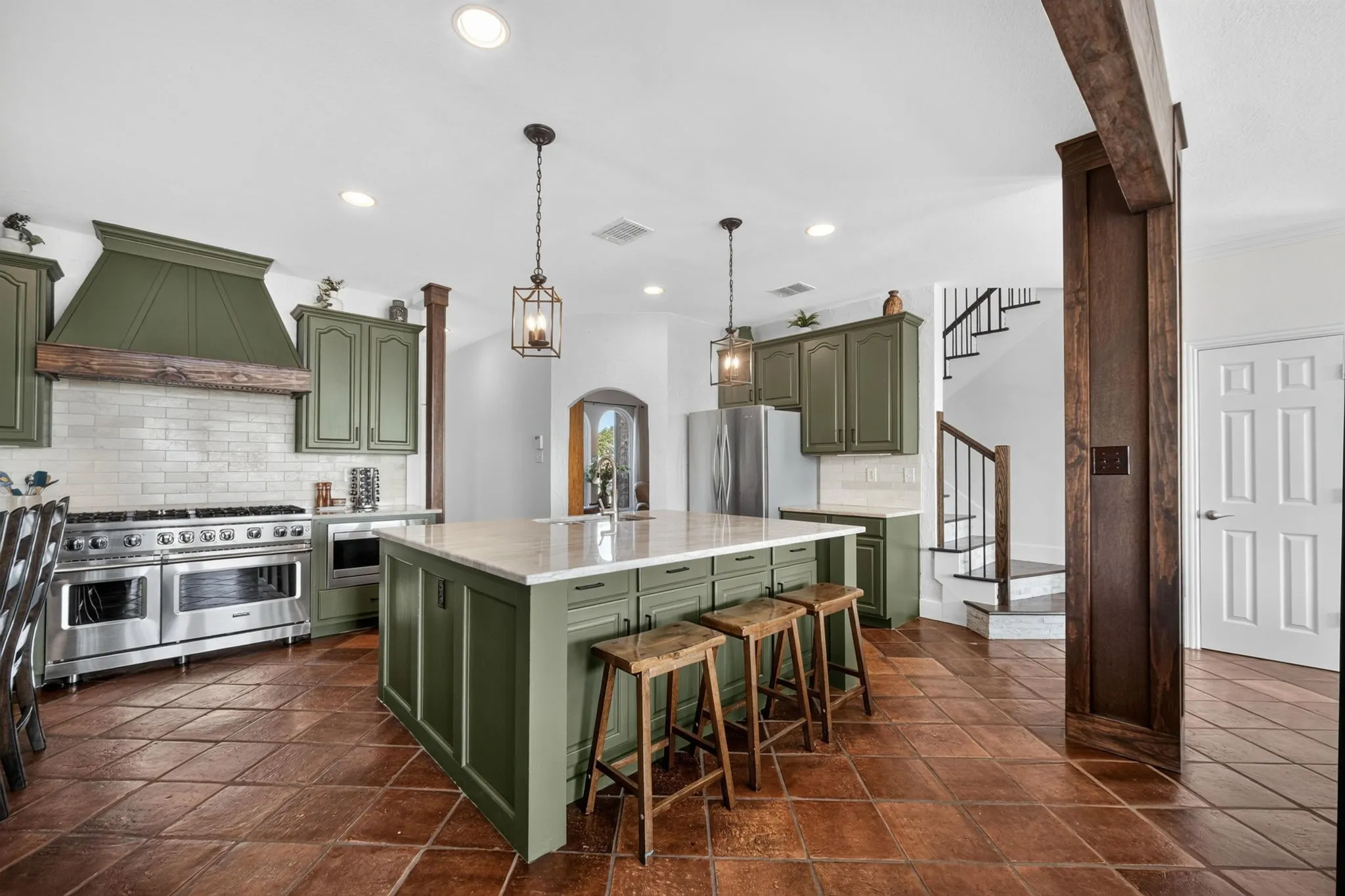 Spacious kitchen featuring an expansive center island, paneled cabinetry, stainless steel appliances, and a tile backsplash