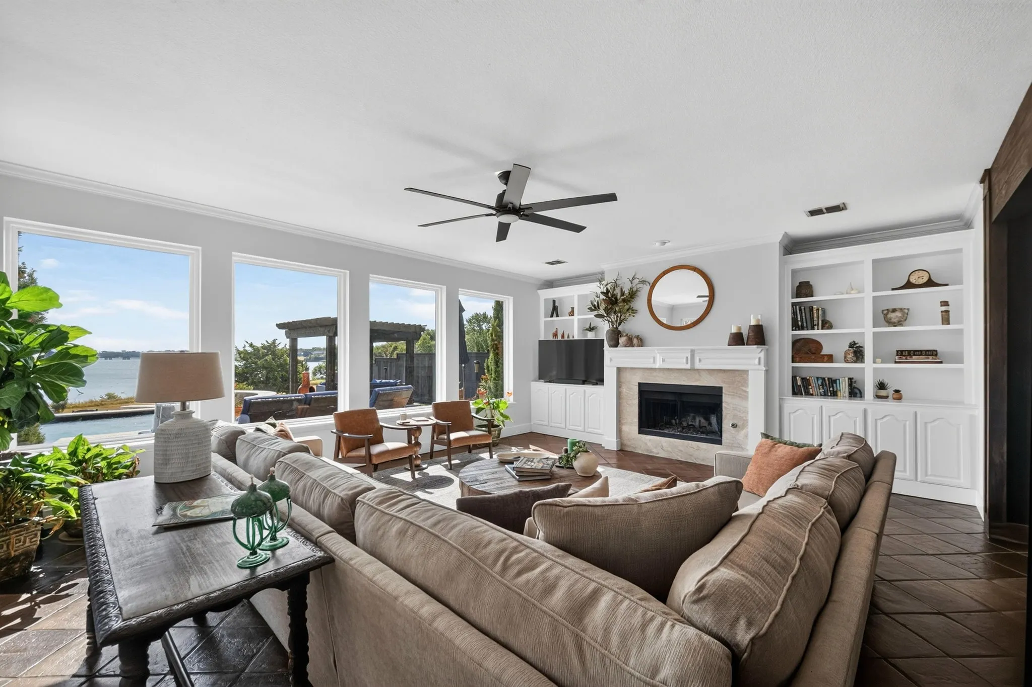 Expansive living area with multiple large windows, a built-in fireplace with mantle, integrated shelving and cabinetry, and a ceiling fan