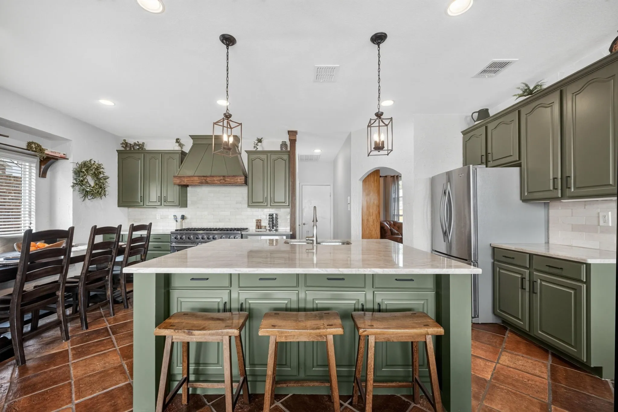 Kitchen featuring green cabinetry, a central island with countertop seating, stainless steel appliances, and a tile backsplash