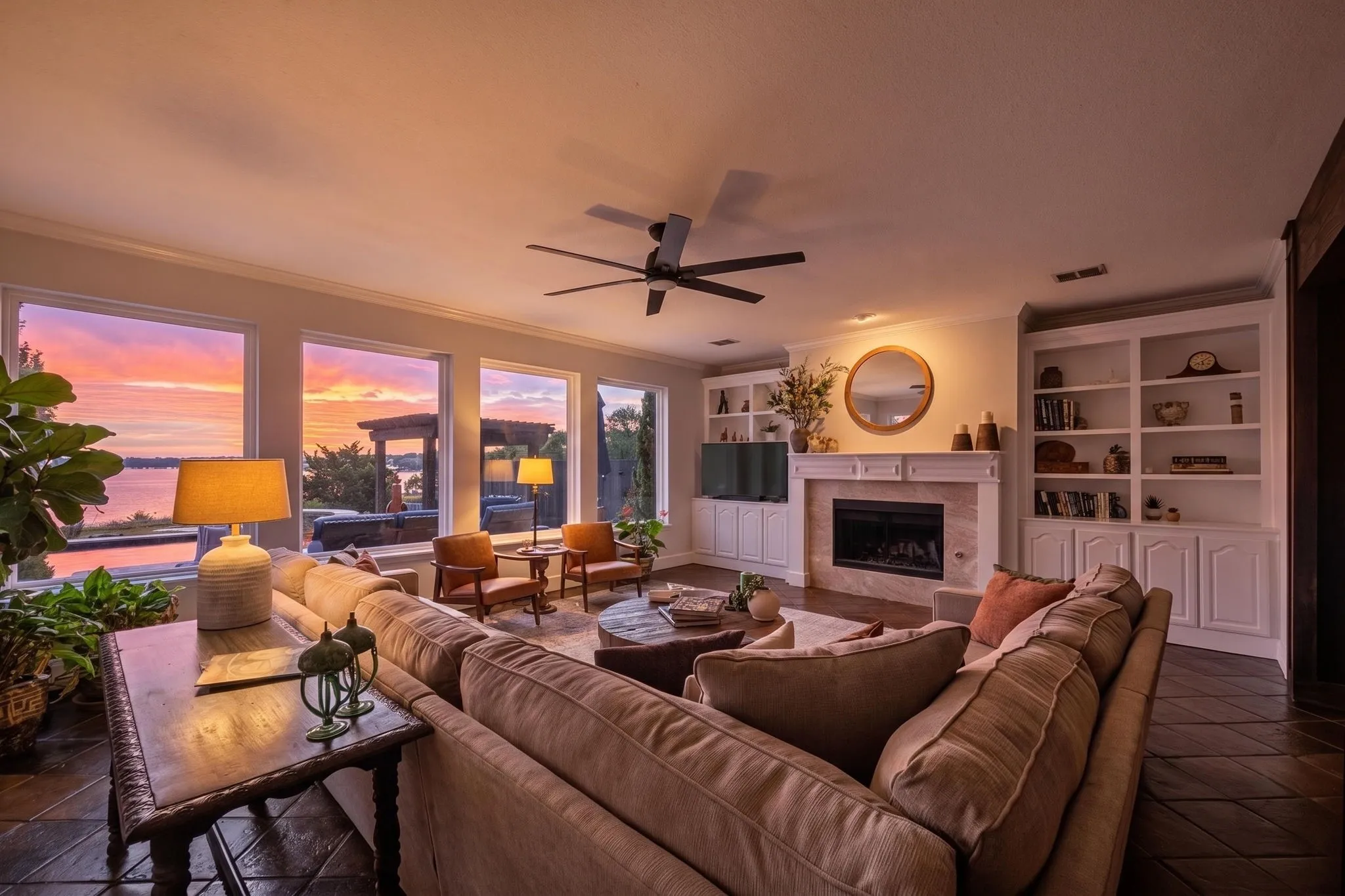 Spacious living area featuring large windows, a fireplace with a mantel, built-in shelving, and a ceiling fan