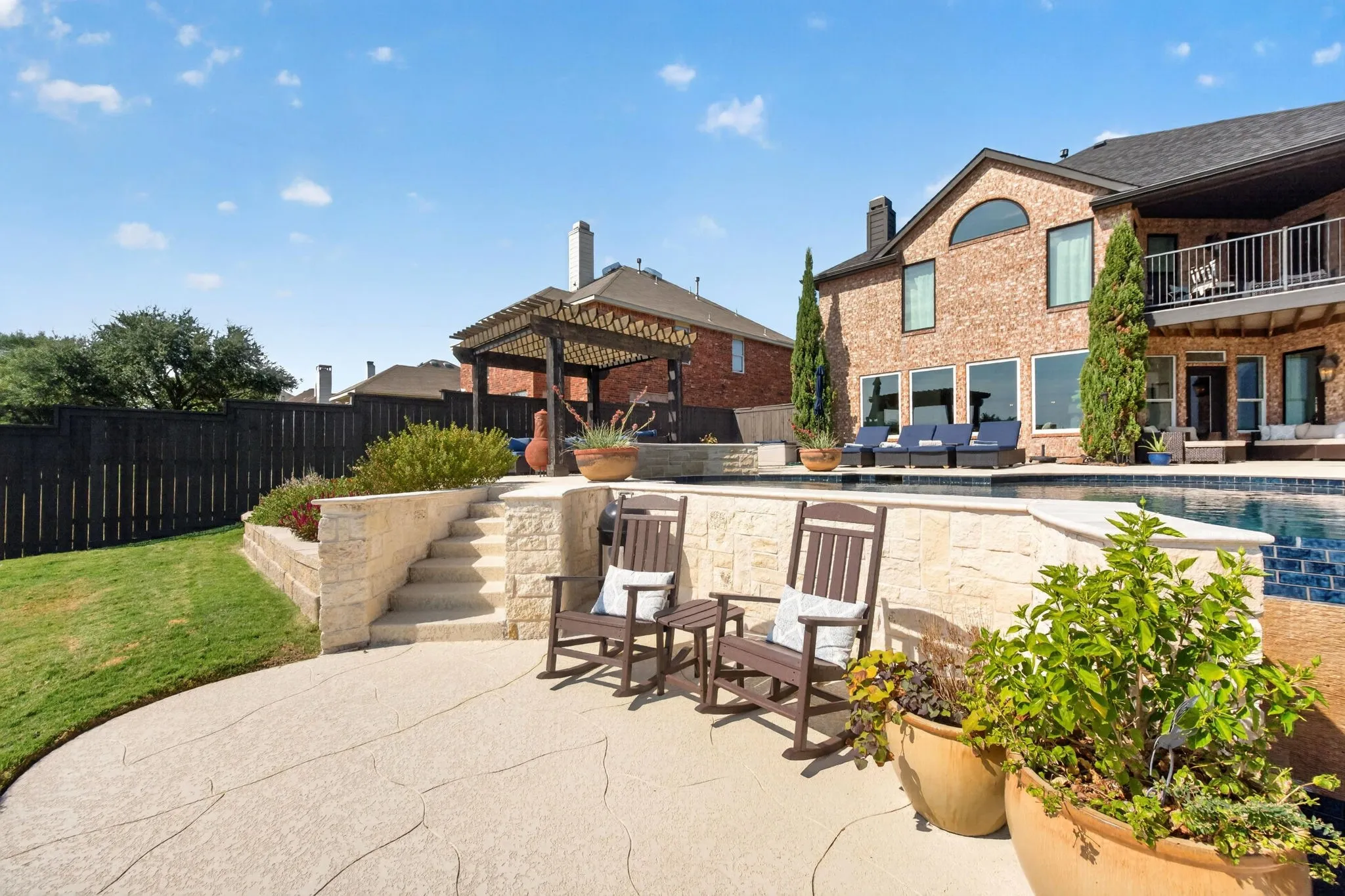 Expansive backyard featuring a custom pool, tiered stone retaining walls, a stamped concrete patio, and a privacy fence