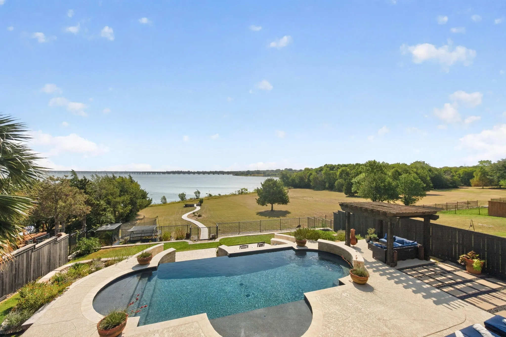 Waterfront property featuring a custom-shaped swimming pool, pergola with a built-in seating area, paved patio, and a fenced yard