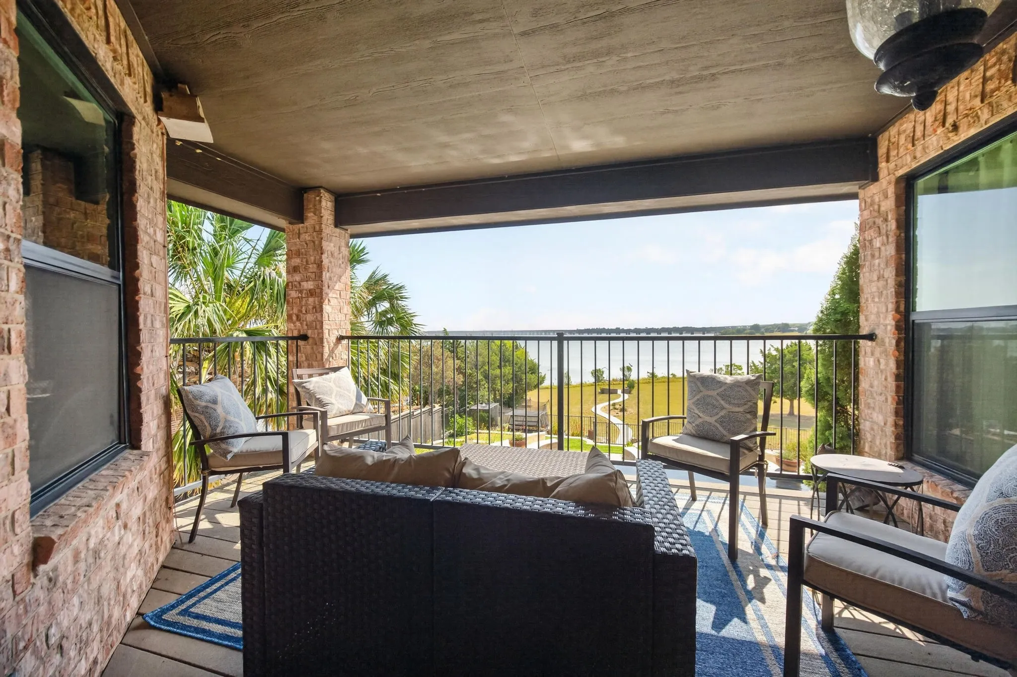 Upstairs covered patio with a metal railing, overlooking a Lake Ray Hubbard, pool, and green landscape.