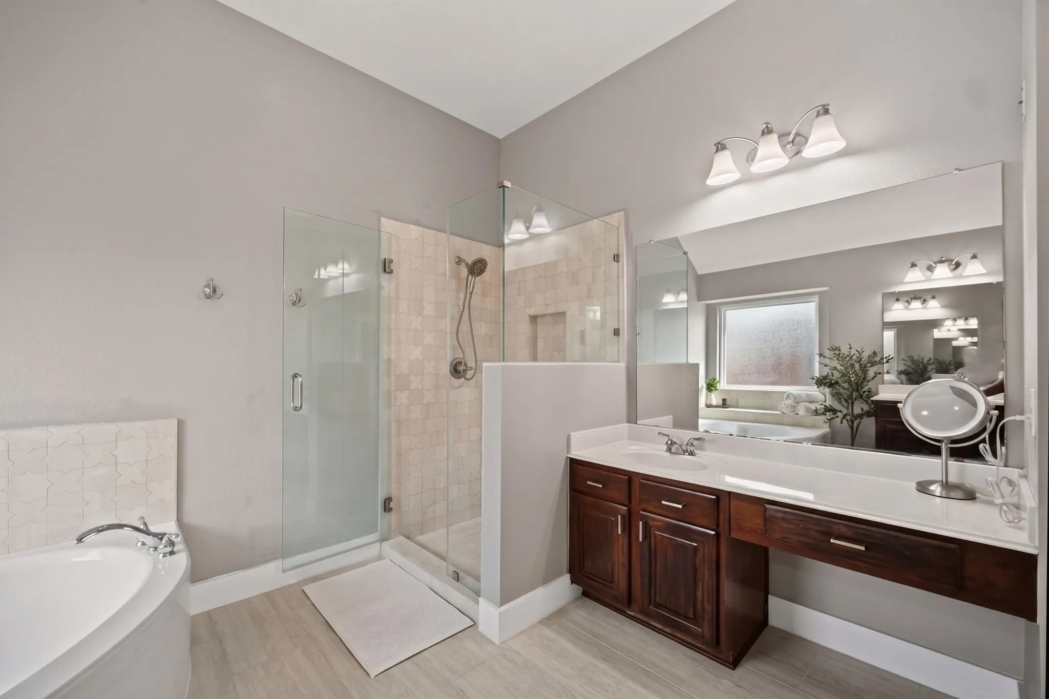 Glass-enclosed shower with tile surround, corner soaking tub, wood-finish vanity with countertop, and large wall-mounted mirror