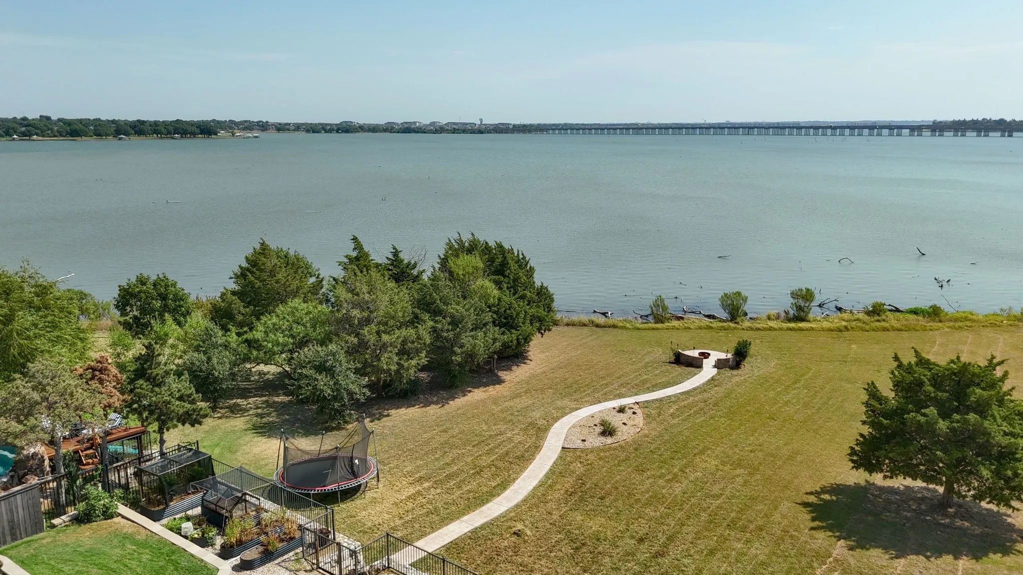 Lakefront property featuring a stone patio with a built-in fire pit, a winding stone pathway, and mature trees