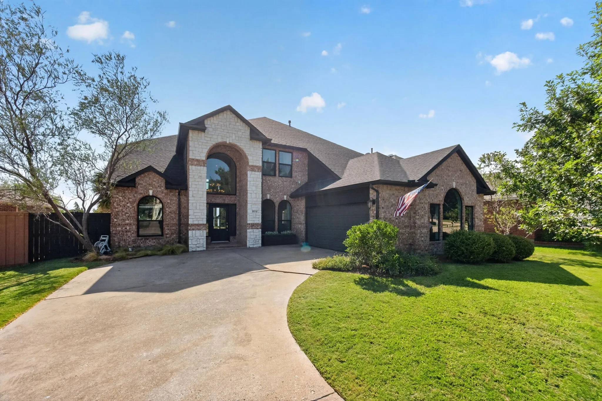 Brick and stone facade, arched entryway, large arched window, attached garage, and a curved concrete driveway