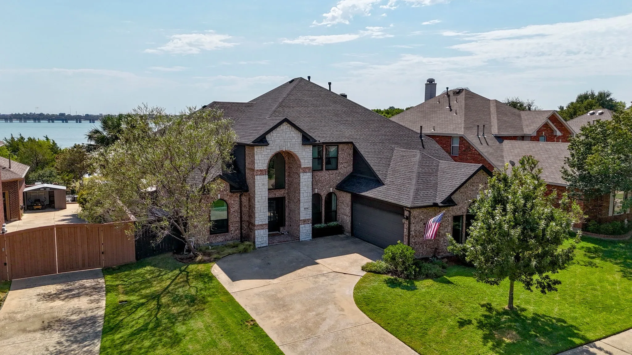 Brick and stone facade with an arched entry, mature landscaping, and a two-car garage