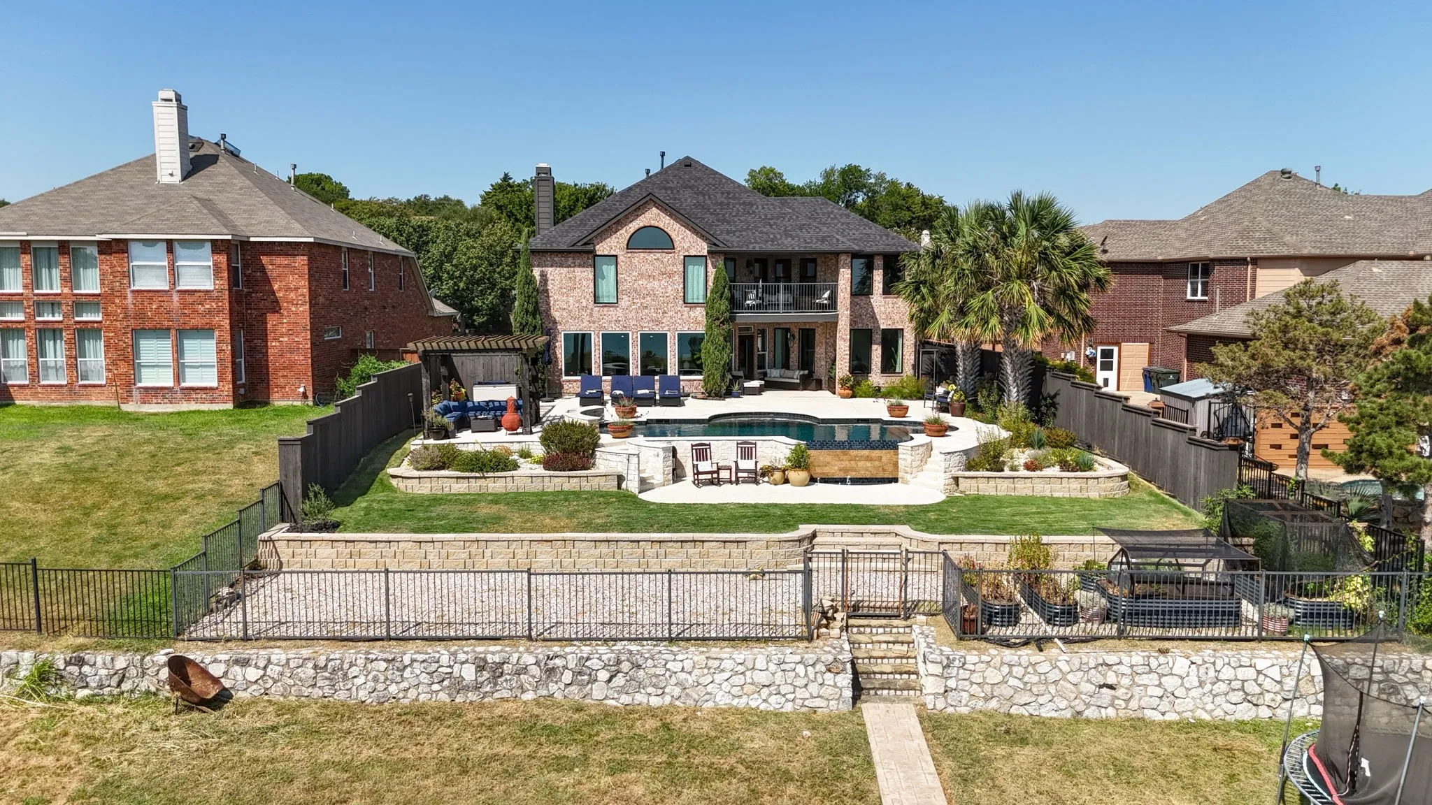 Brick facade residence with a multi-level backyard featuring a swimming pool, stone retaining walls, and a manicured lawn