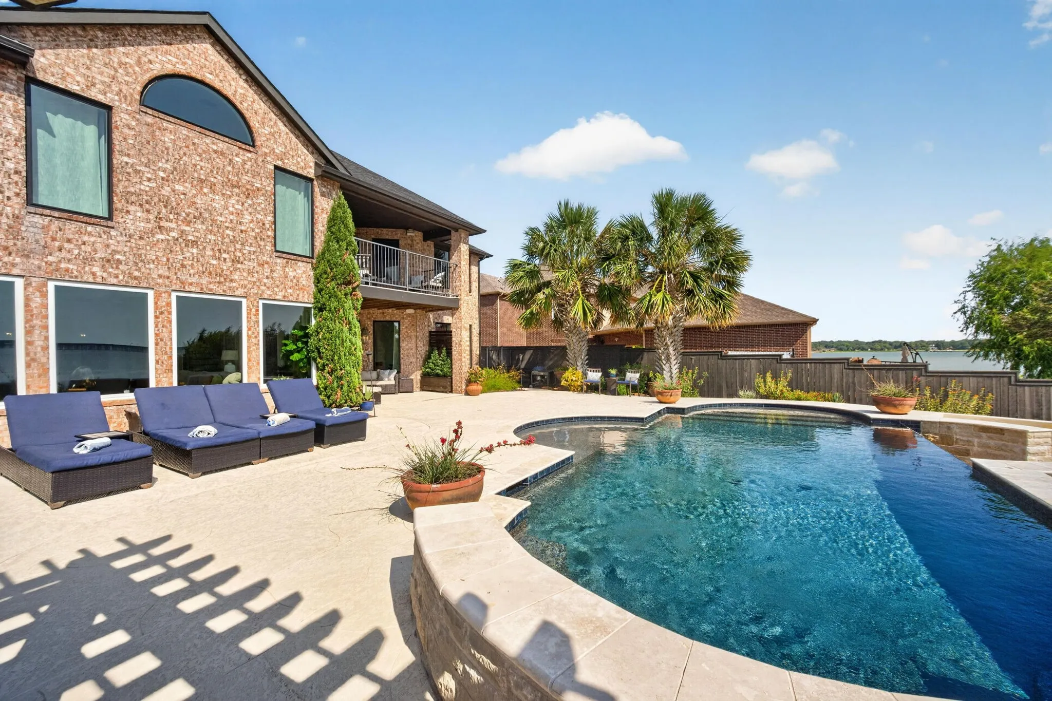 Brick exterior, curved swimming pool, expansive concrete patio, mature palm trees, and an upper-level balcony