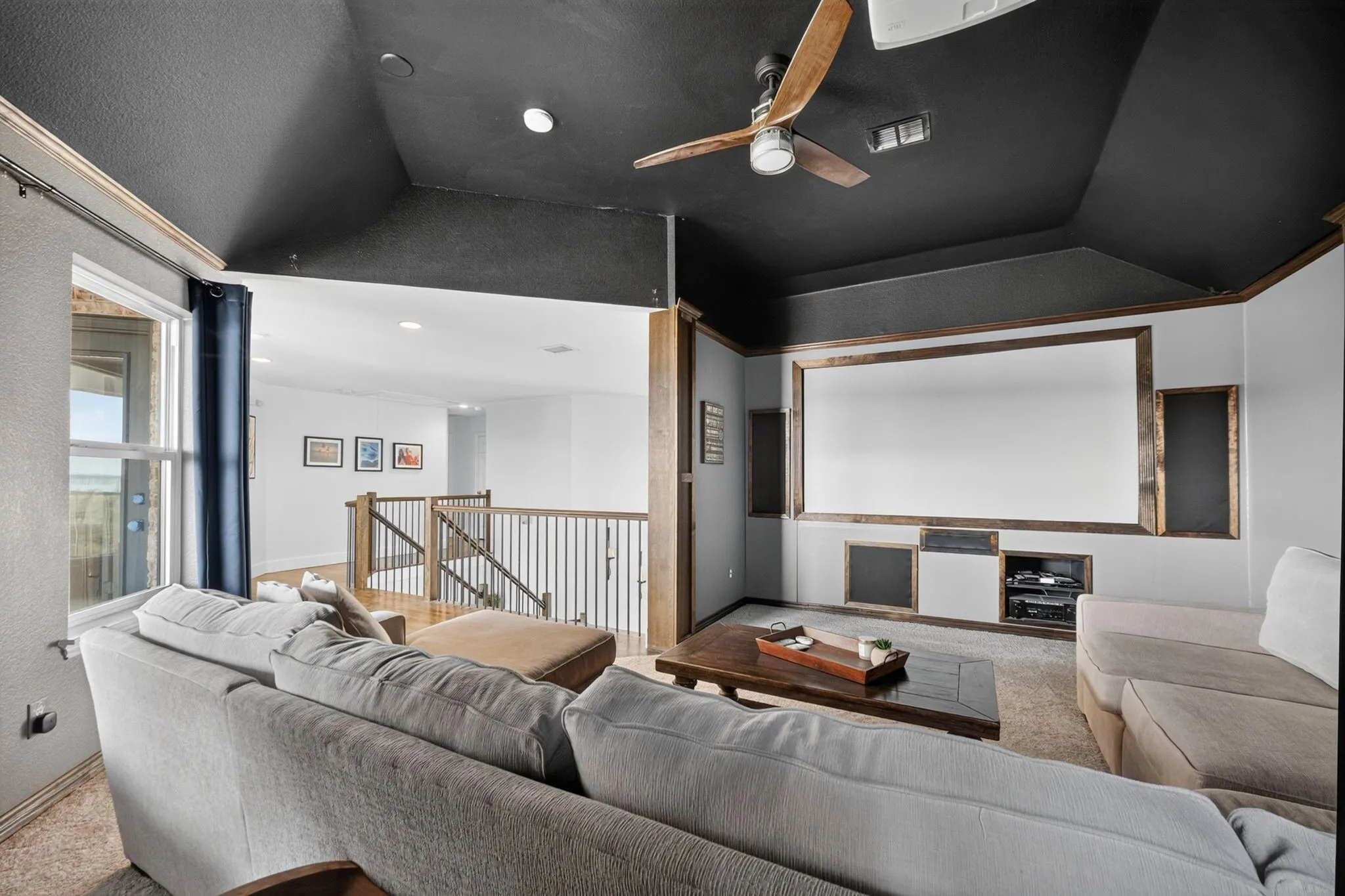 Dedicated media room featuring a large projector screen, built-in media shelving, and a ceiling fan