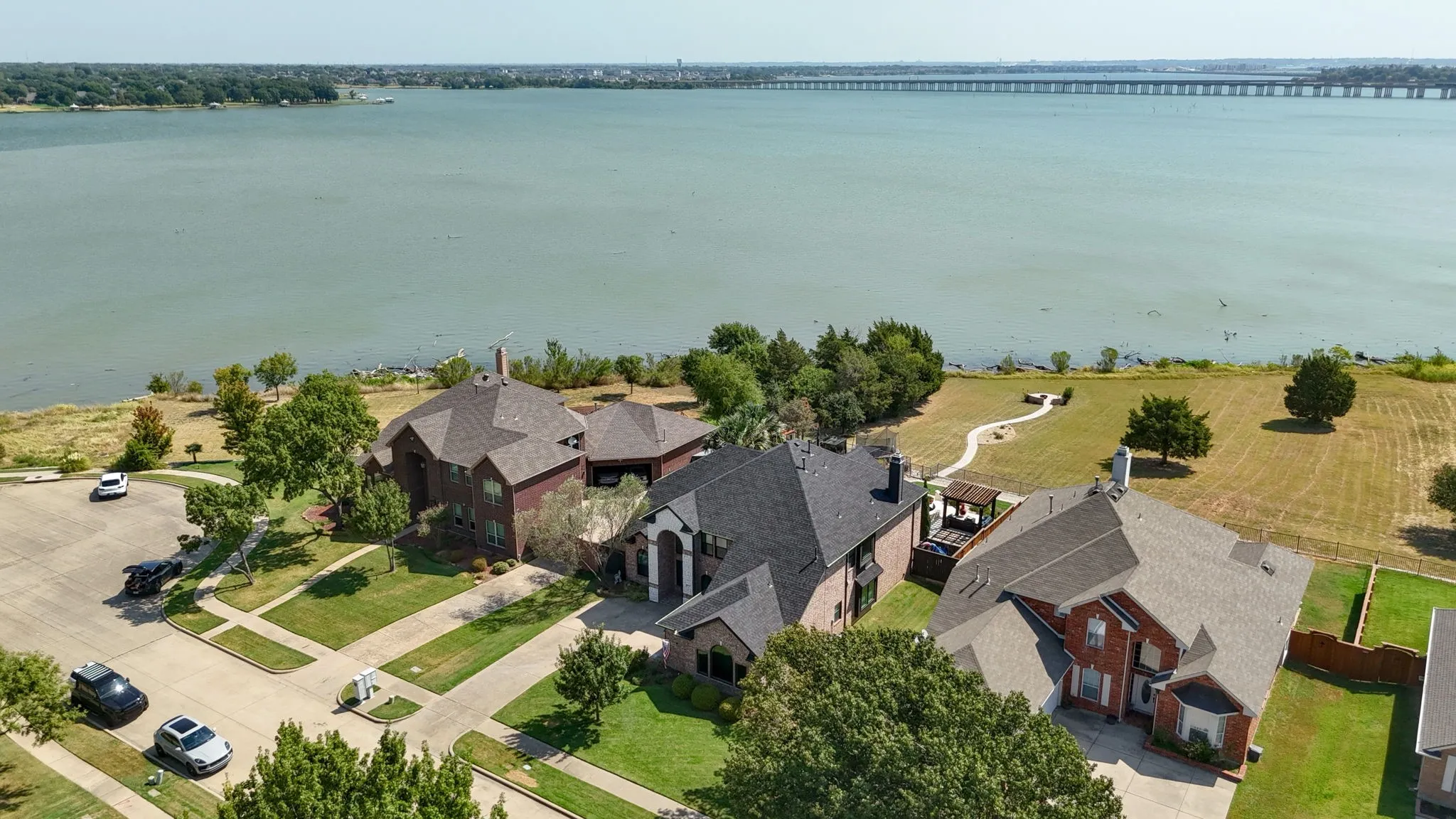 Waterfront property with a large body of water, paved roadways, and mature trees