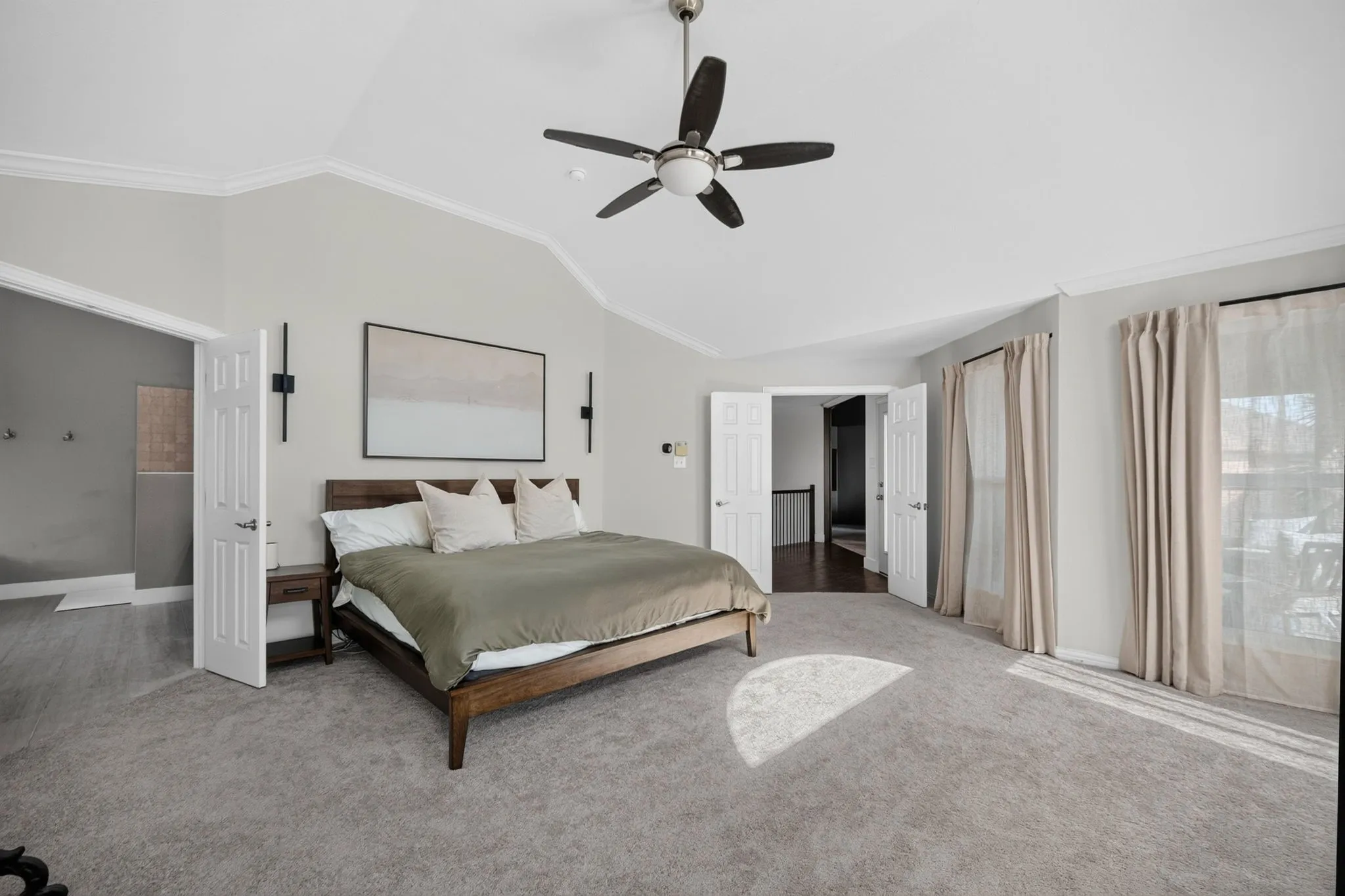 Vaulted ceiling with crown molding, ceiling fan, carpet flooring, and double-panel doors