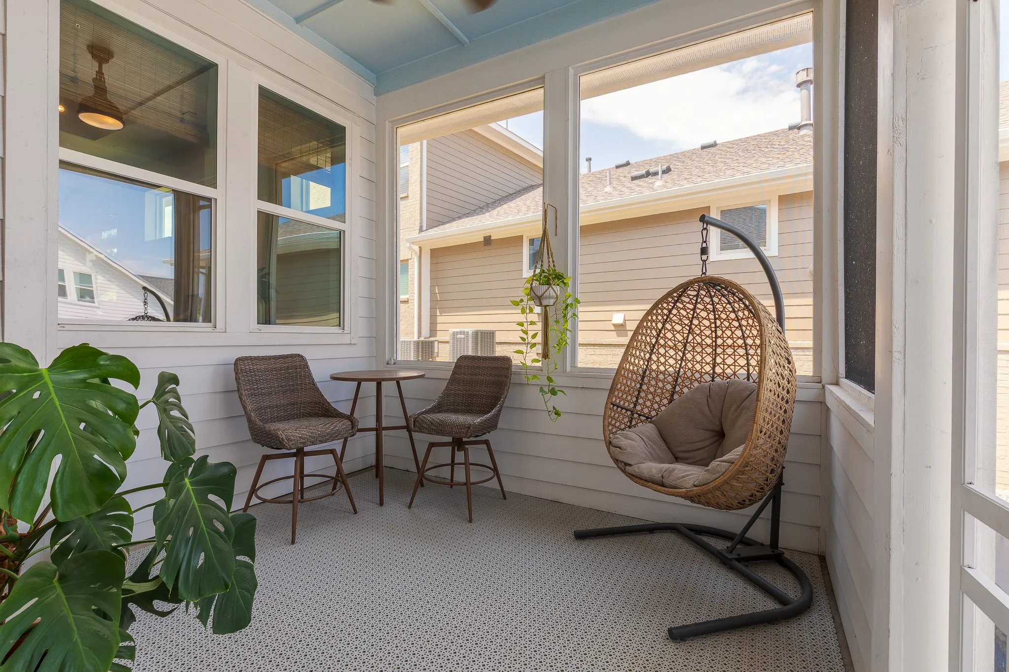 Screened porch with light blue ceiling, white paneled walls, ceiling fan, and light-toned patterned flooring