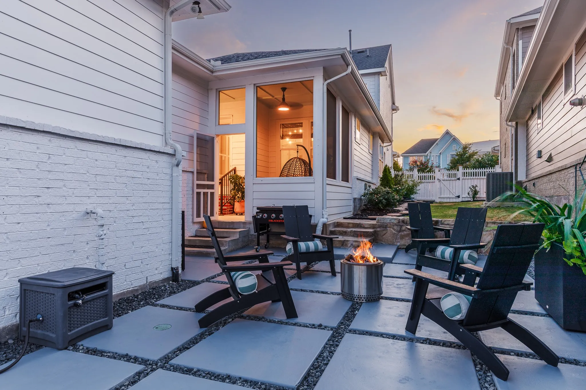 Concrete paver patio with gravel accents, leading to a screened-in porch with ceiling fan and built-in lighting
