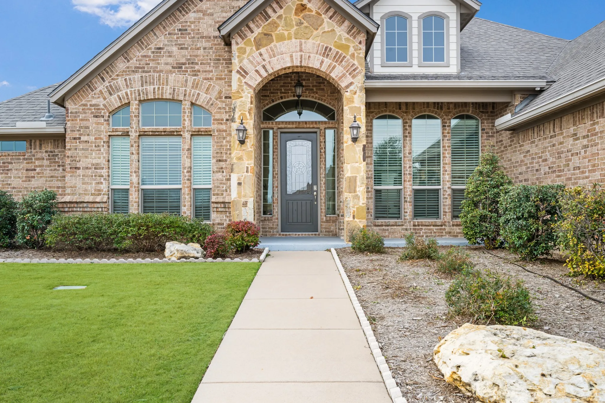 Elegant brick facade featuring a grand arched entryway with sidelights, multiple arched and rectangular windows with stone trim detailing, and a covered entry portico