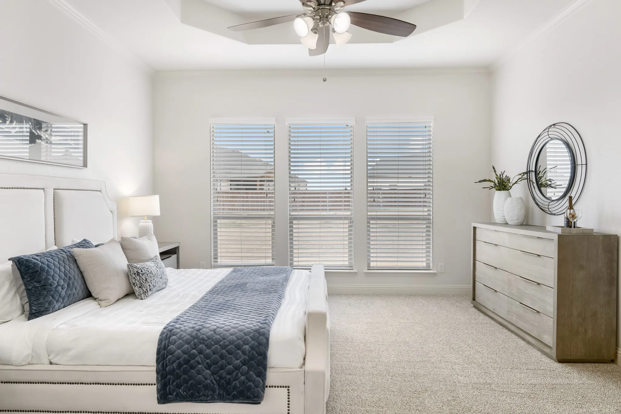 Tray ceiling with a ceiling fan, three windows with horizontal blinds, light-toned carpet flooring, and crown molding