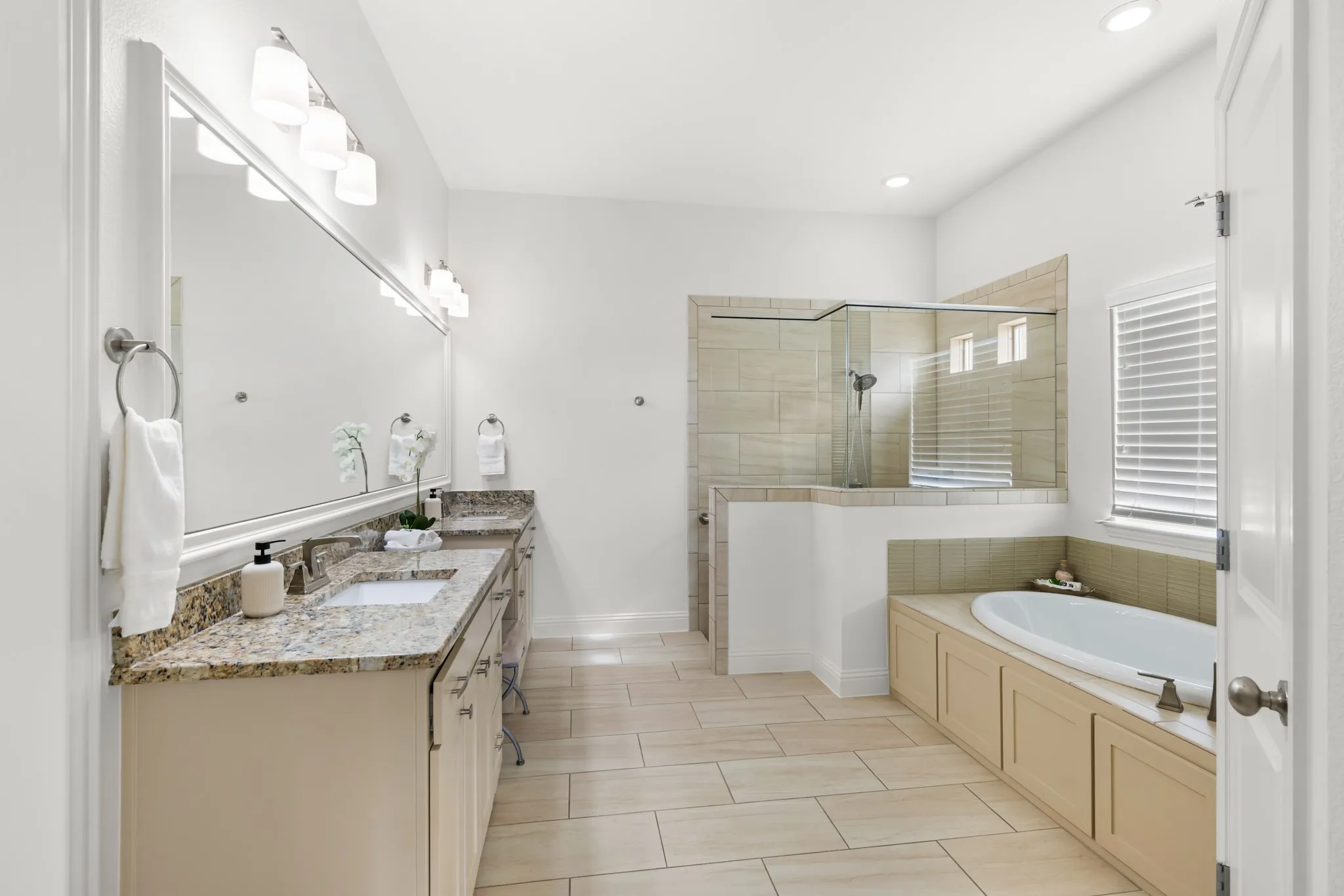 Dual vanity with stone countertops, walk-in shower with glass enclosure, built-in soaking tub, and tile flooring