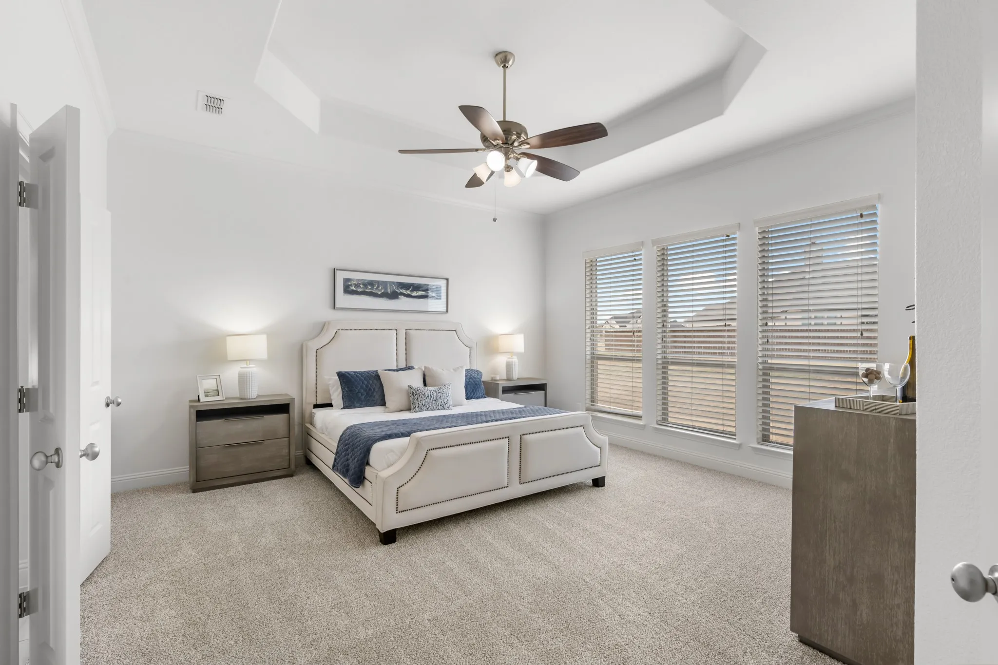 Recessed ceiling with crown molding, ceiling fan, triple windows with horizontal blinds, and neutral carpeting