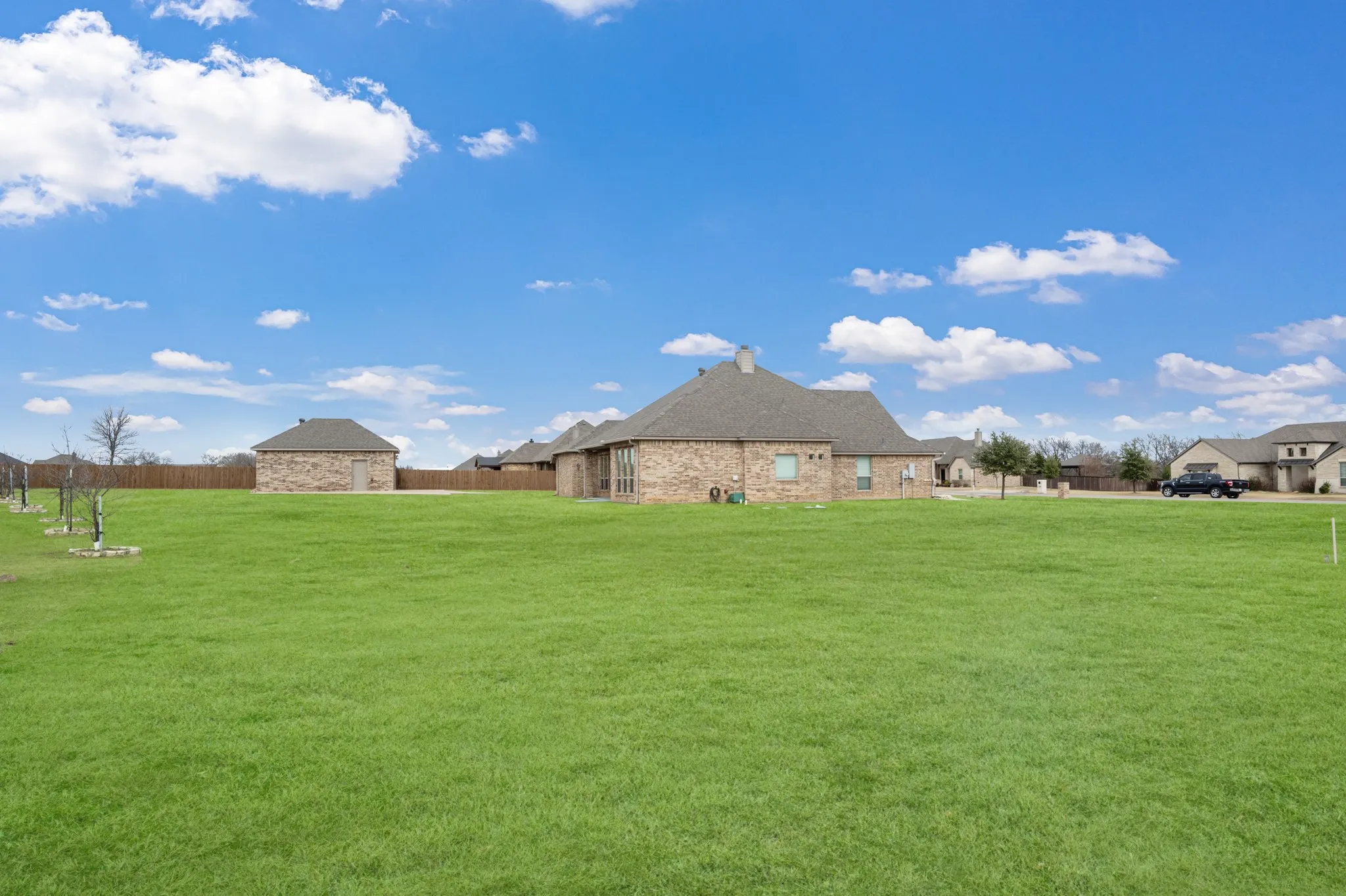 Expansive manicured lawn with mature landscaping and stone residential structures featuring pitched rooflines set against open countryside backdrop