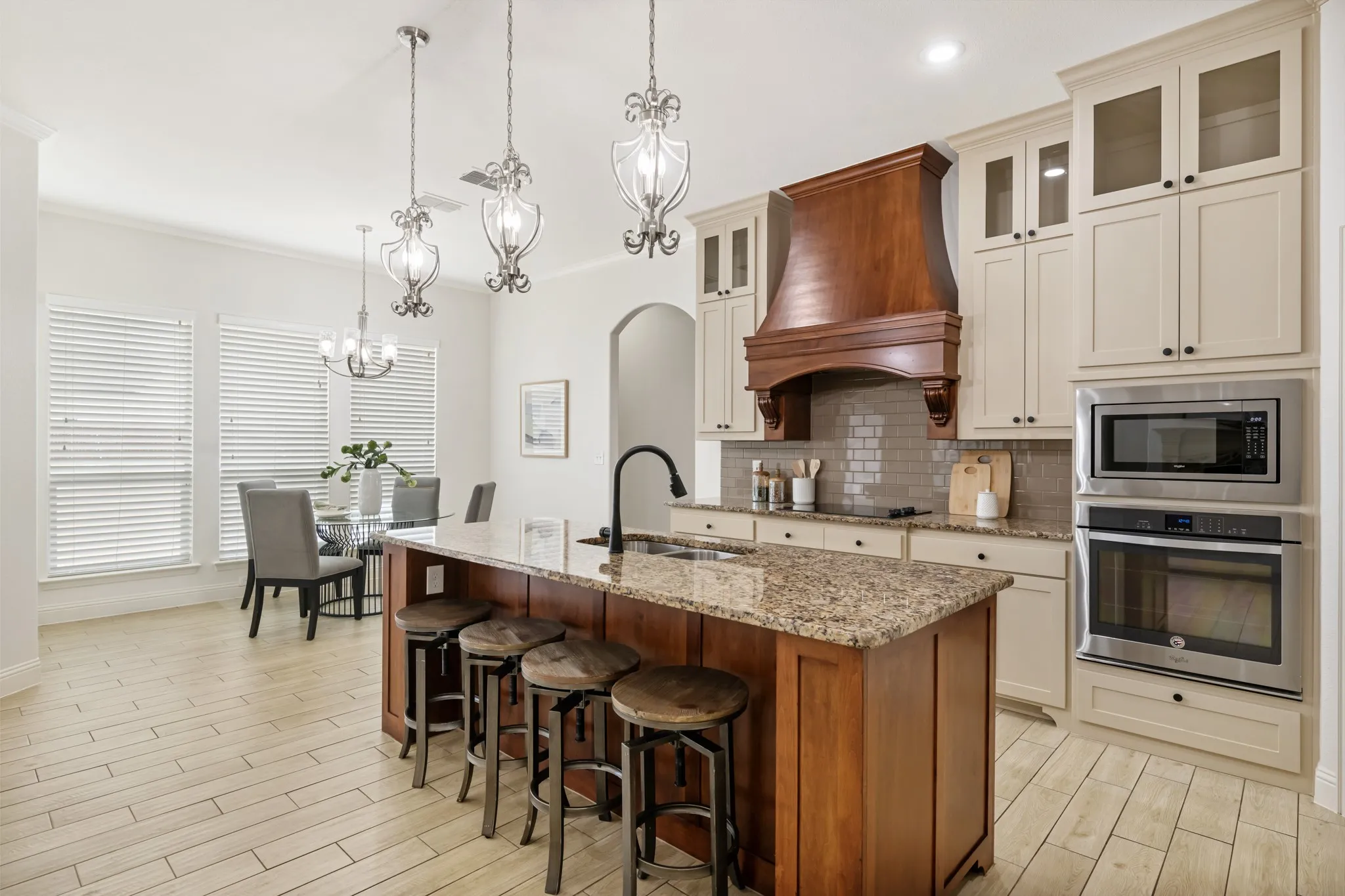 Gourmet kitchen featuring a two-tier island with wood-finish cabinetry and granite countertops, paired with cream-painted perimeter cabinetry and glass-front upper cabinets