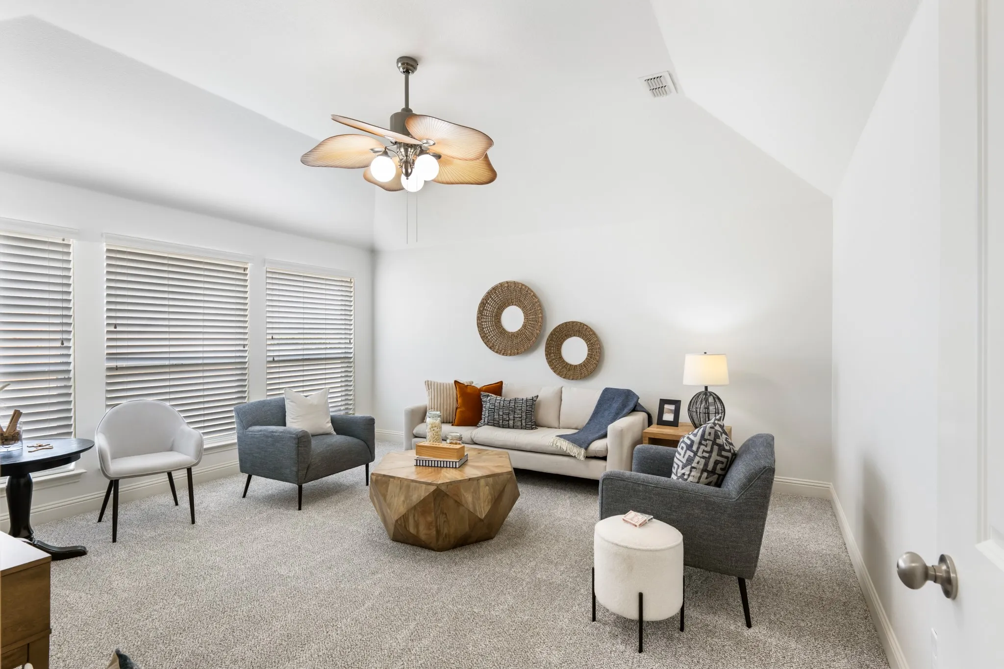 Vaulted ceiling with a tropical-style ceiling fan, multiple windows with blinds, and neutral carpeting