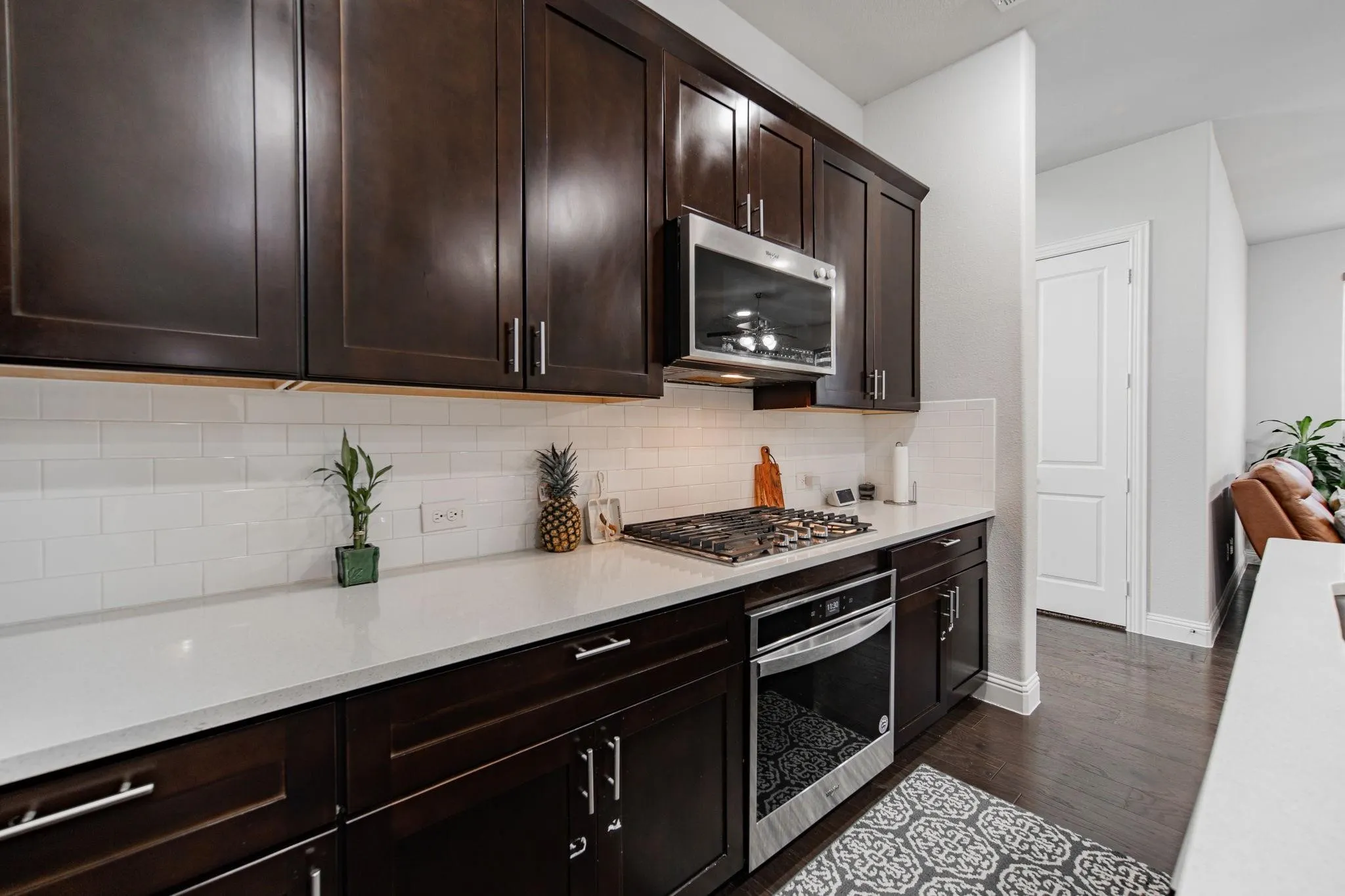 Dark wood-finish cabinetry, stainless steel microwave, gas cooktop, white subway tile backsplash, and light-toned countertops