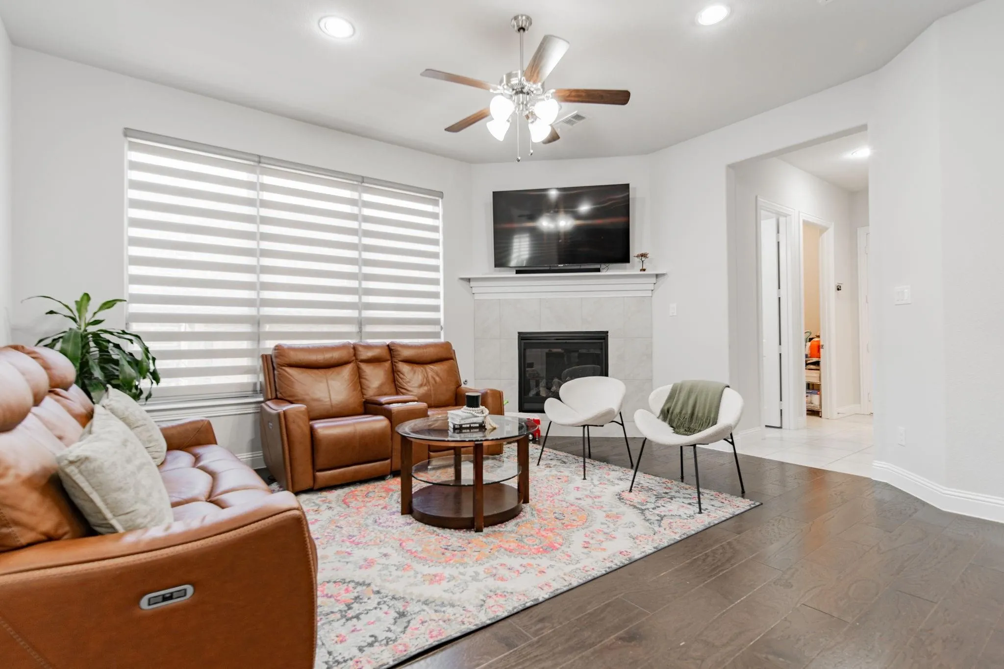 Spacious living area featuring wood-finish flooring, a ceiling fan, recessed lighting, and a fireplace with a mantel