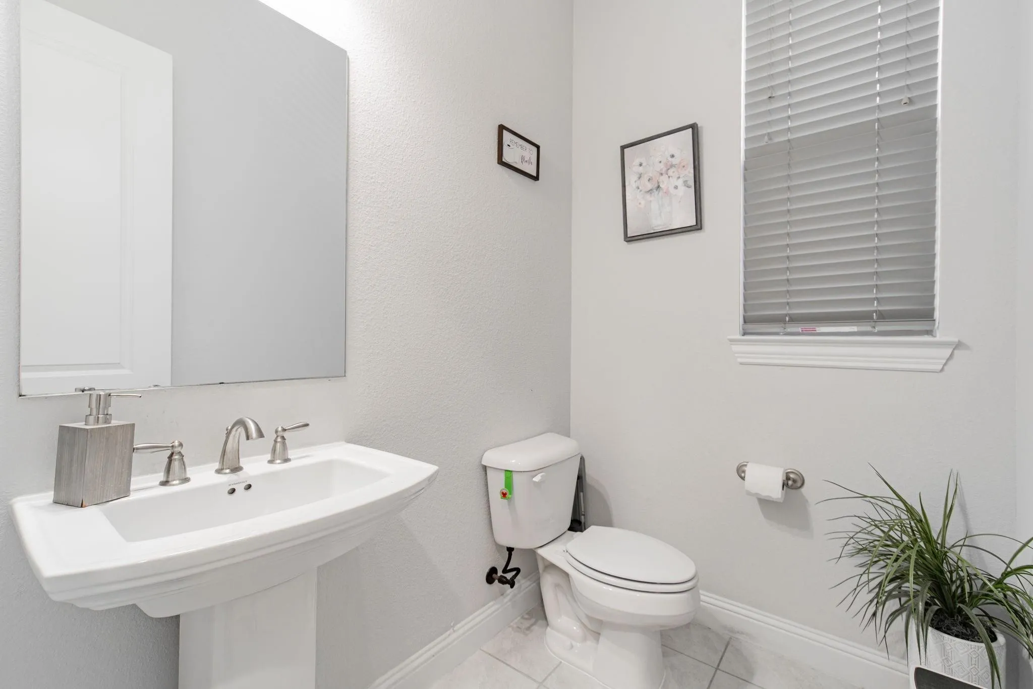 Pedestal sink with brushed nickel faucet, wall-mounted mirror, and a window with blinds