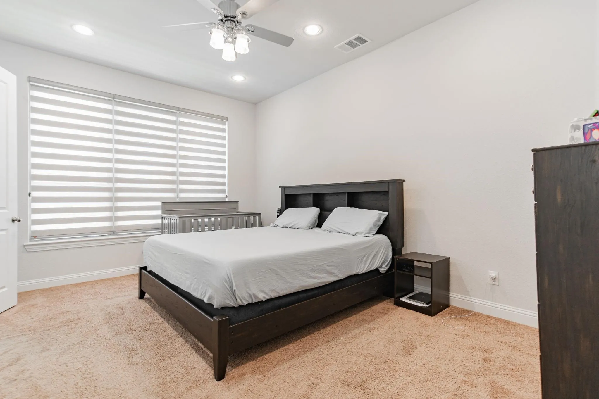 Spacious primary bedroom featuring a dark wood platform bed frame, warm wood-finish flooring, and abundant natural light from large horizontal-slat shuttered windows