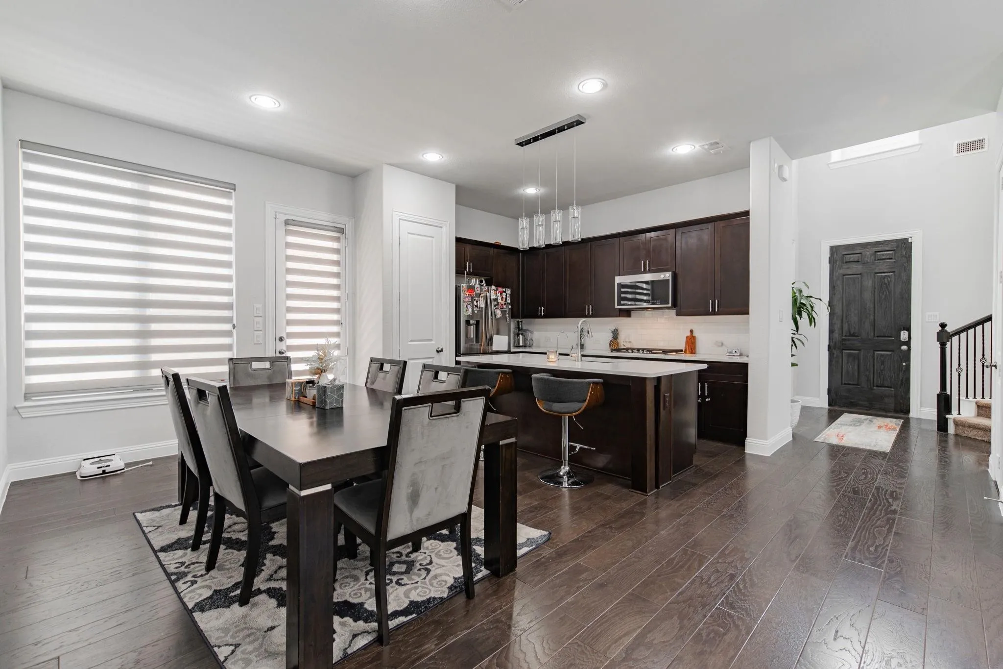 Wood-finish flooring throughout, kitchen with dark wood cabinetry, stainless steel appliances, a center island with countertop seating, and recessed lighting