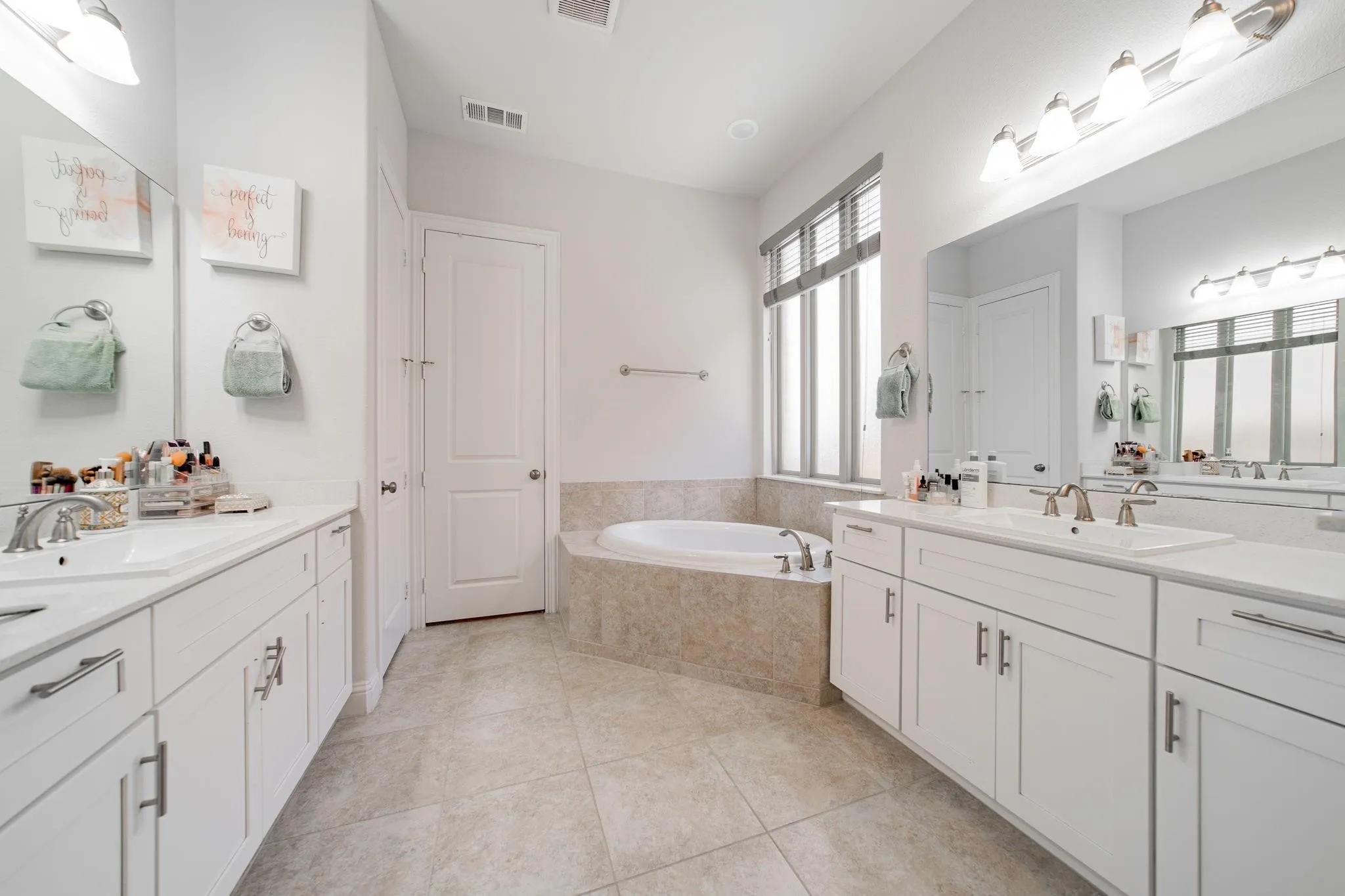 Spa-inspired primary bathroom featuring dual vanities with white cabinetry, marble-finish countertops, and polished chrome fixtures