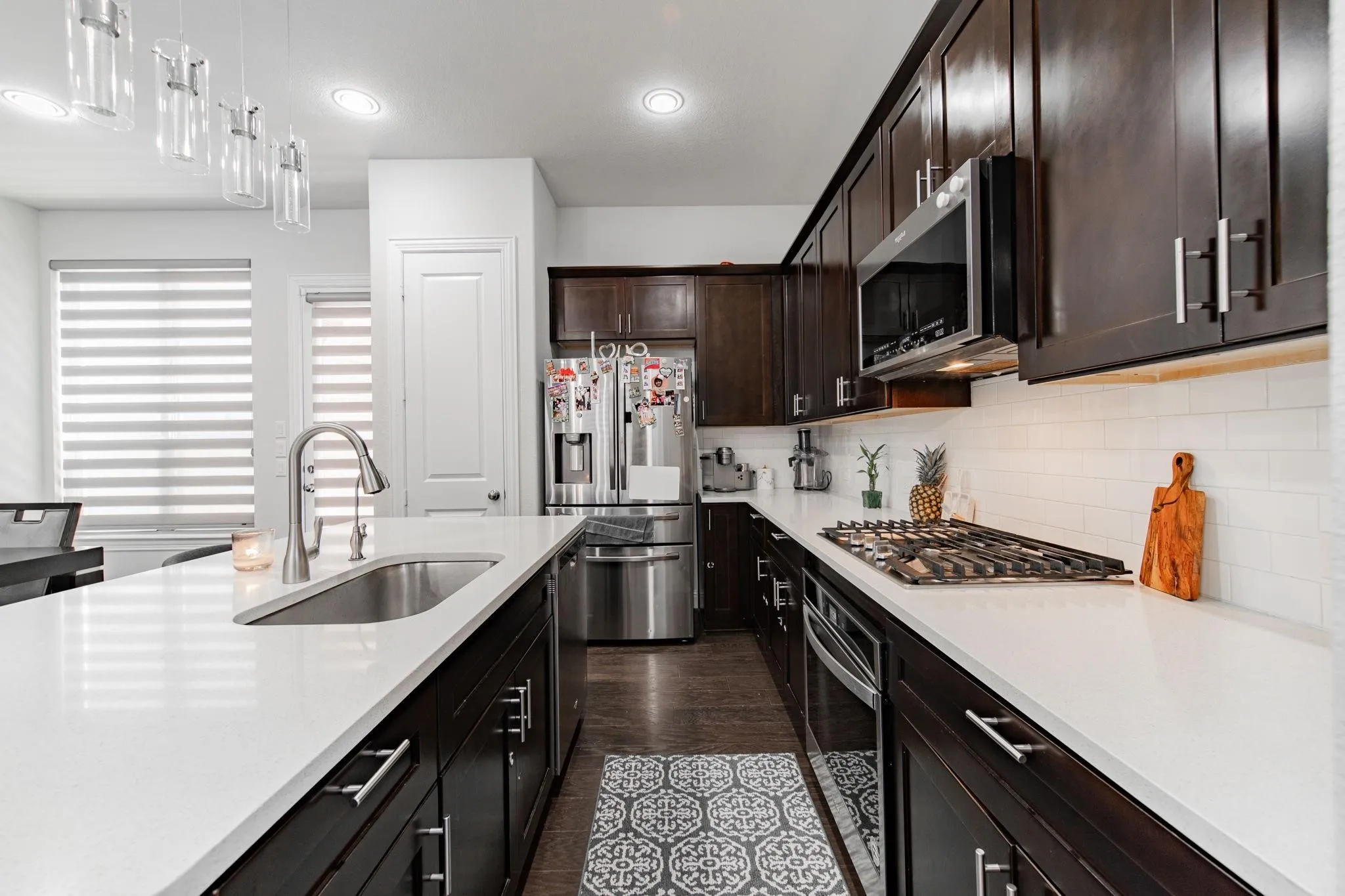 Contemporary kitchen featuring dark wood cabinetry, white countertops, stainless steel appliances, a gas cooktop, and a subway tile backsplash